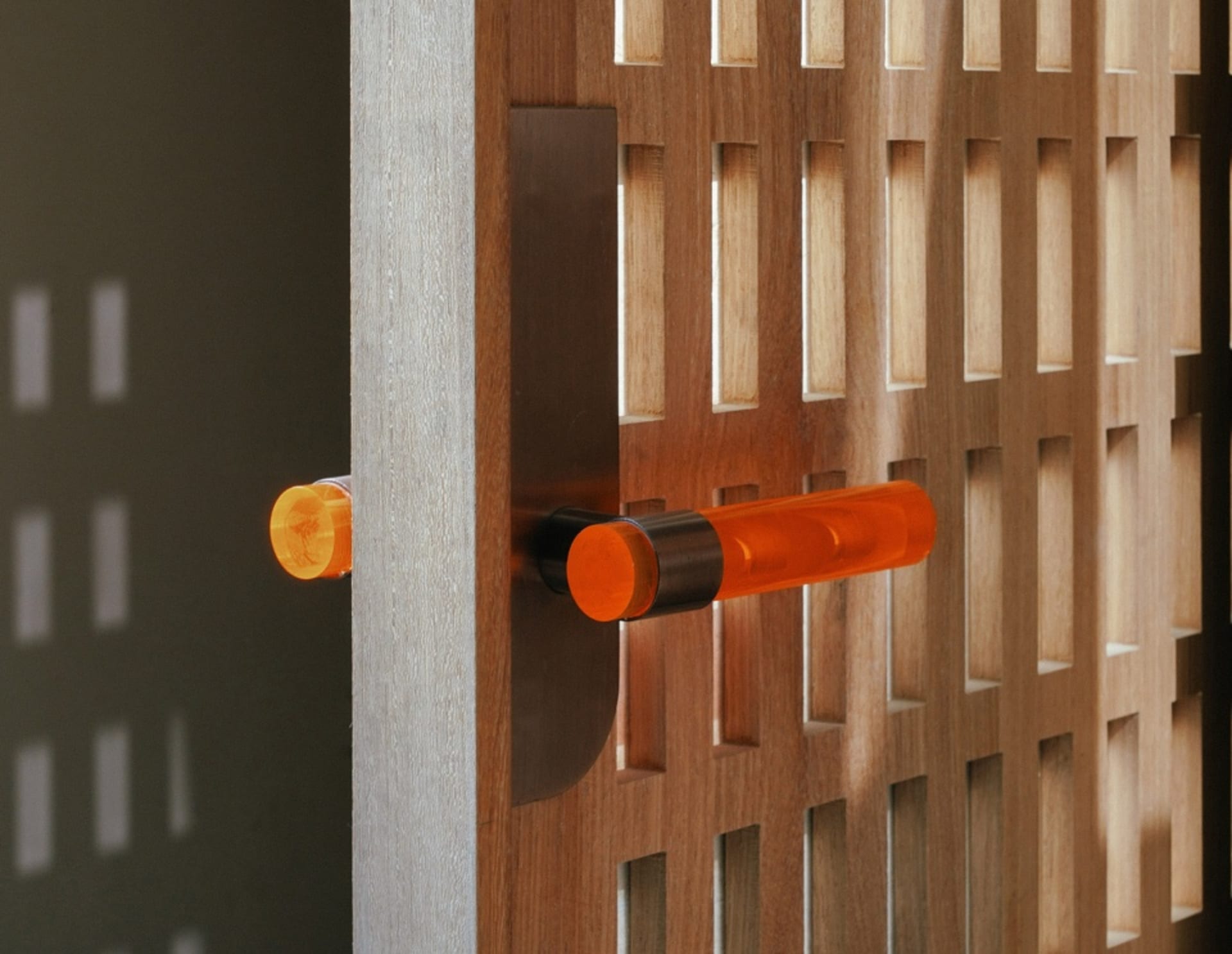 An orange acrylic door handle attached to a wooden grid door.