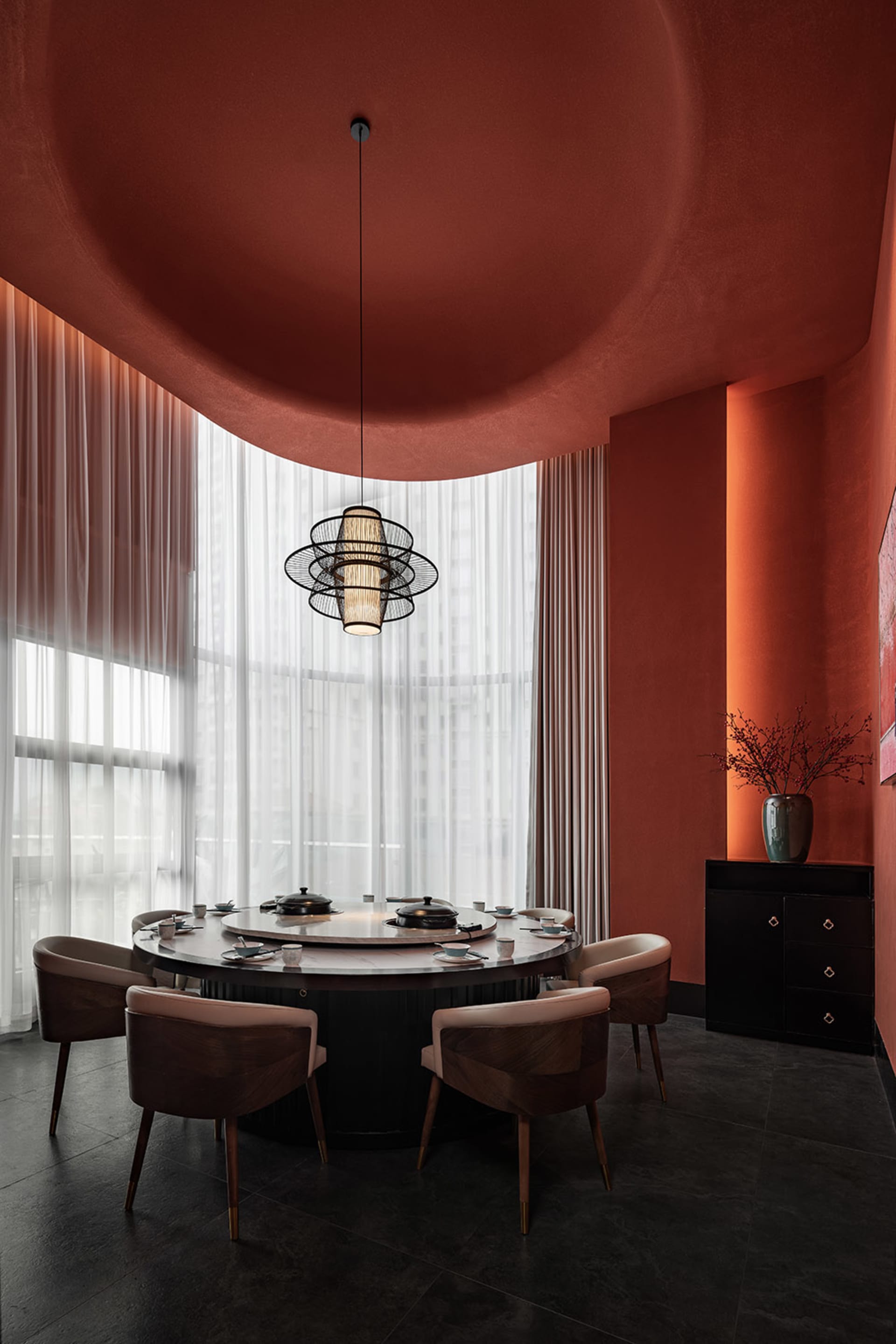 A modern dining room with a metallic table centerpiece, wooden chairs, and sheer textiles for soft lighting.