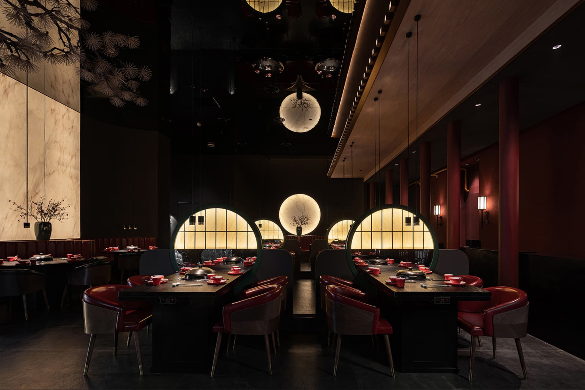 A modern restaurant interior with dark wooden tables and chairs, circular glass windows, and red leather seats.