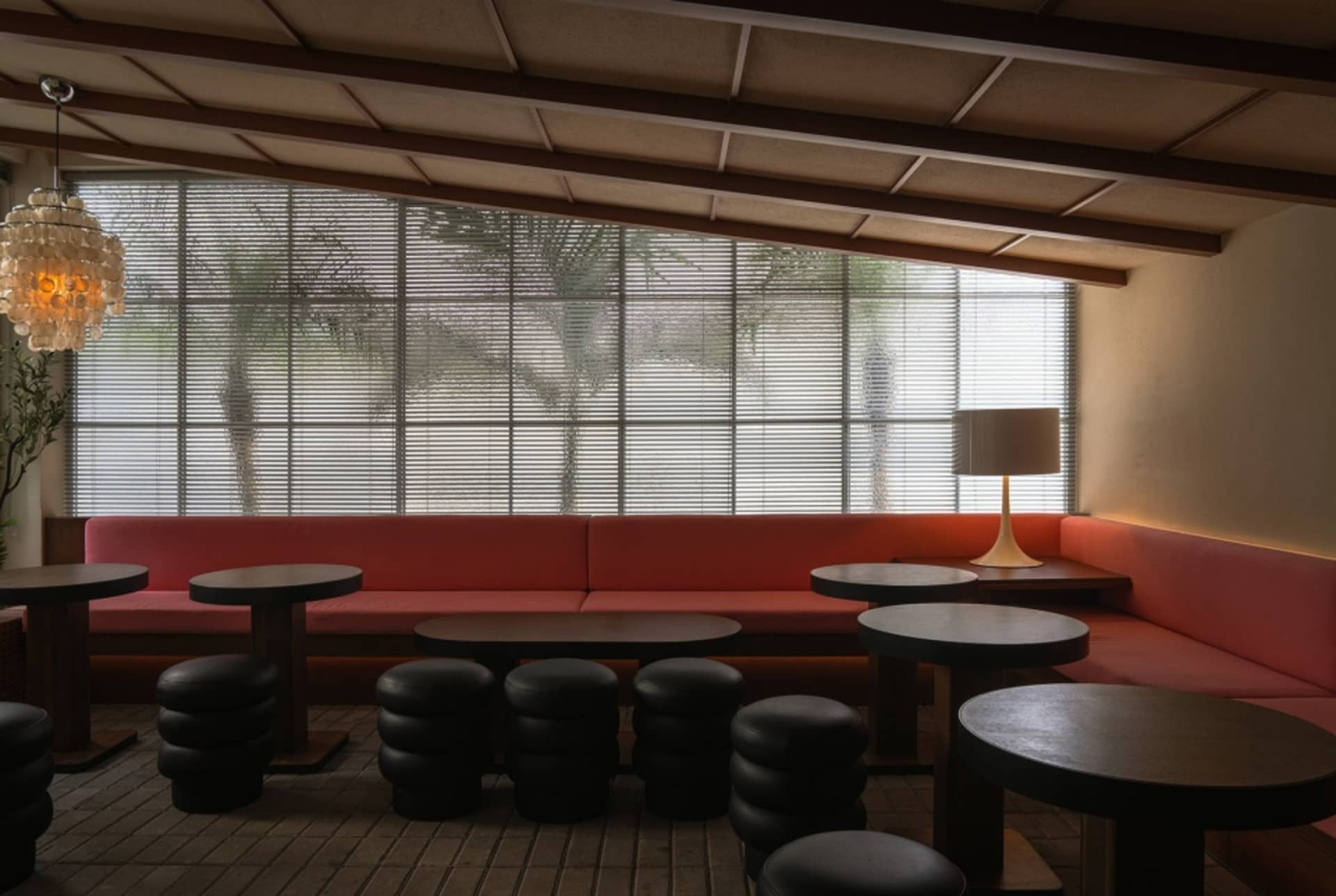 Modern restaurant interior with fabric seating, wood tables, metal stools, and plants.