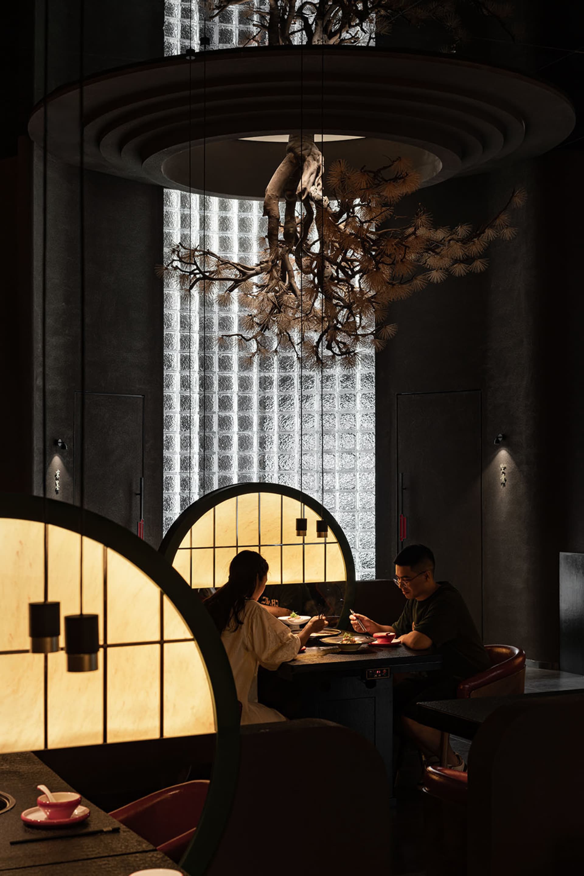 A modern restaurant interior with wooden seating, warm lighting, and concrete walls.