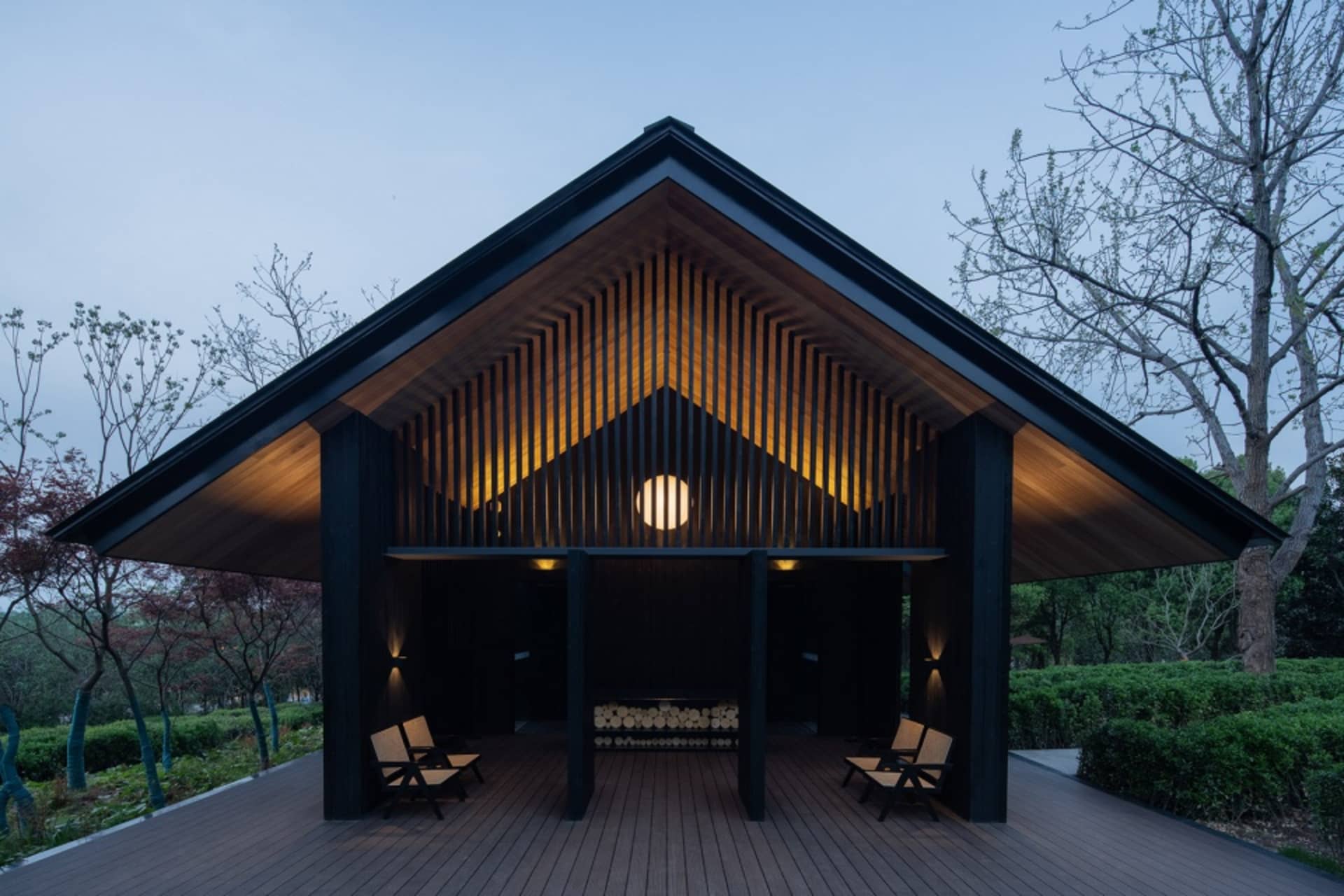 A modern architectural structure featuring a black wooden exterior with illuminated wood slats and seating area.