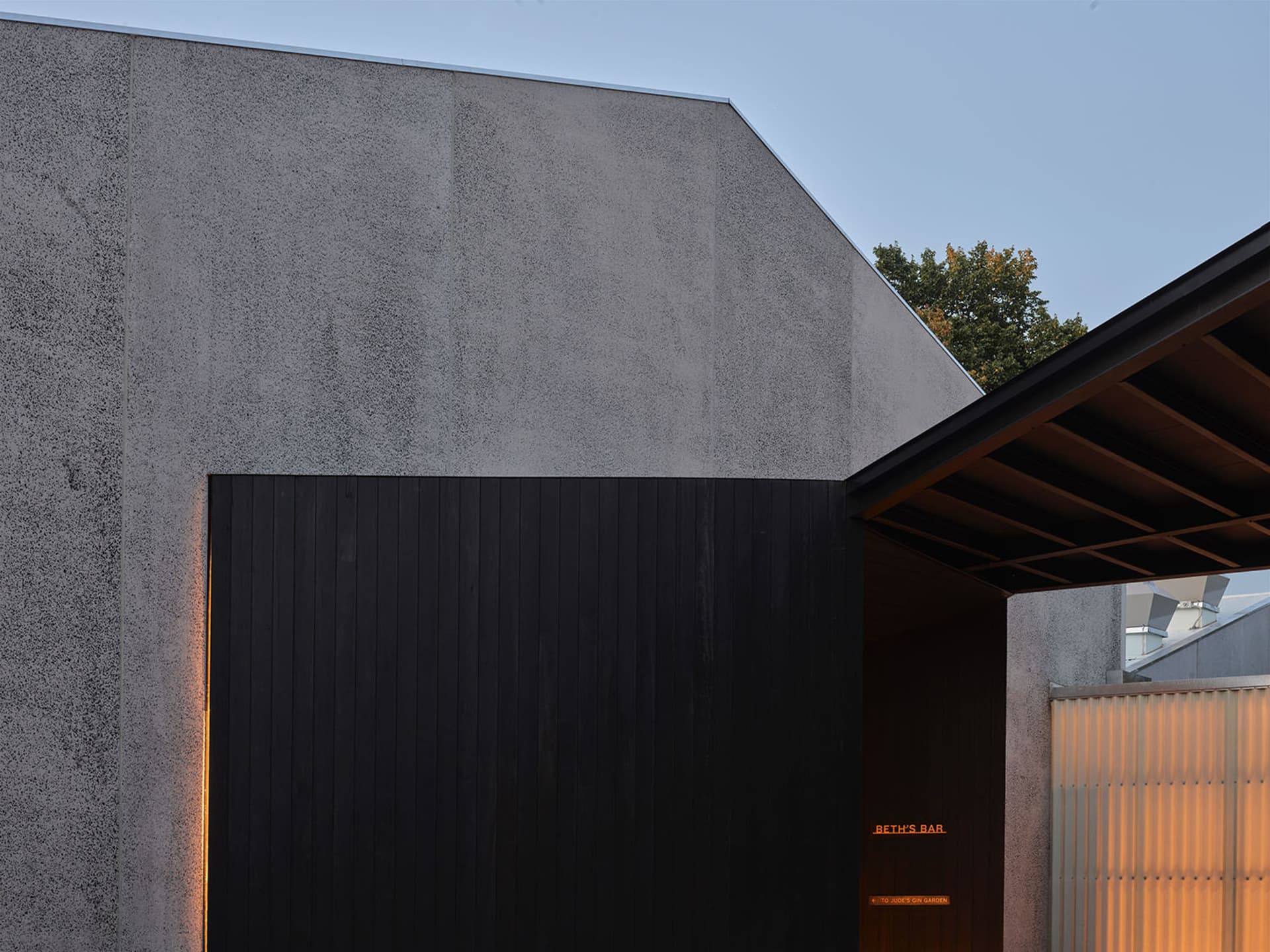Modern concrete exterior facade with a black wall and orange-lit signage indicating 'Beth's Bar'.