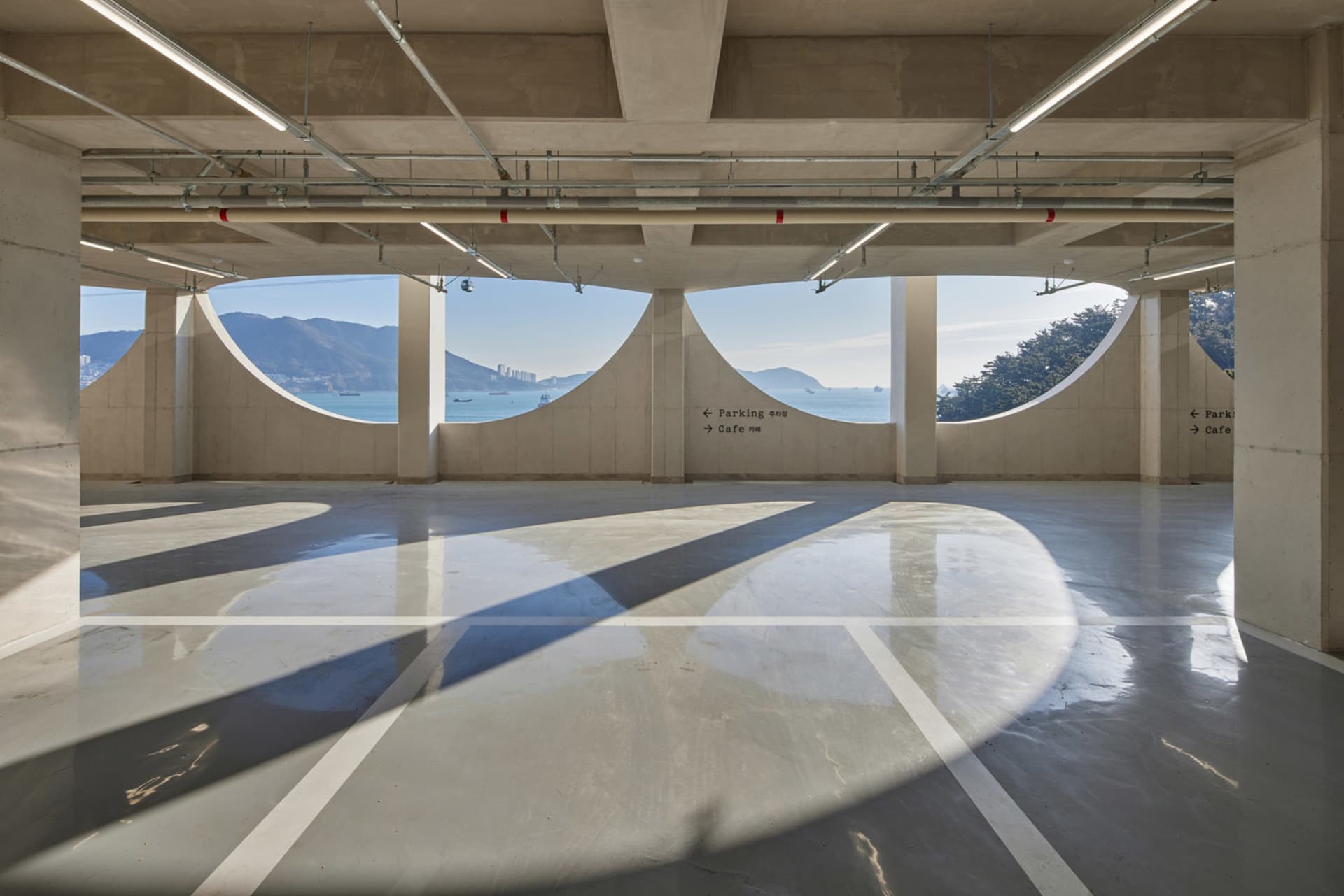 A spacious, modern parking garage interior with concrete walls and arched windows overlooking the ocean.