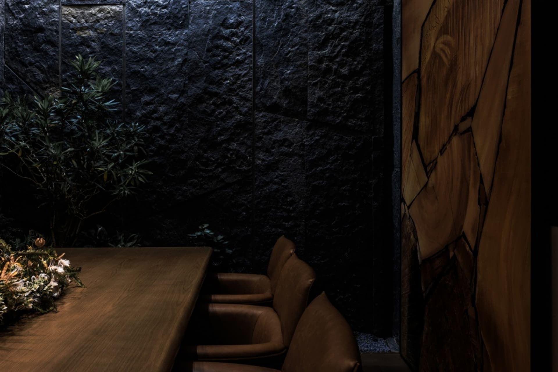 Industrial style restaurant interior with black stone walls, wooden table, and leather chairs.
