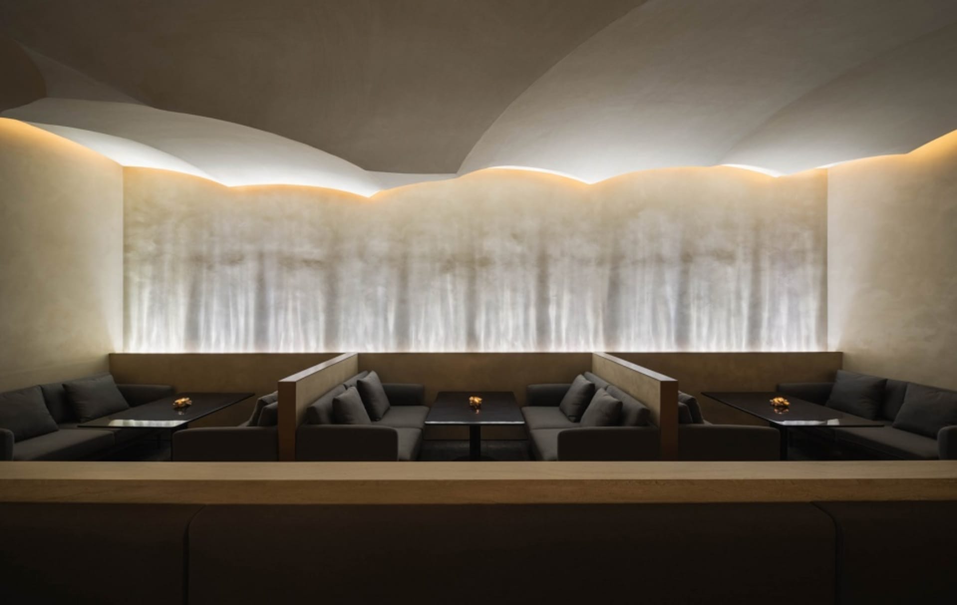 Modern restaurant bar with dark tables, black couches, and illuminated wall