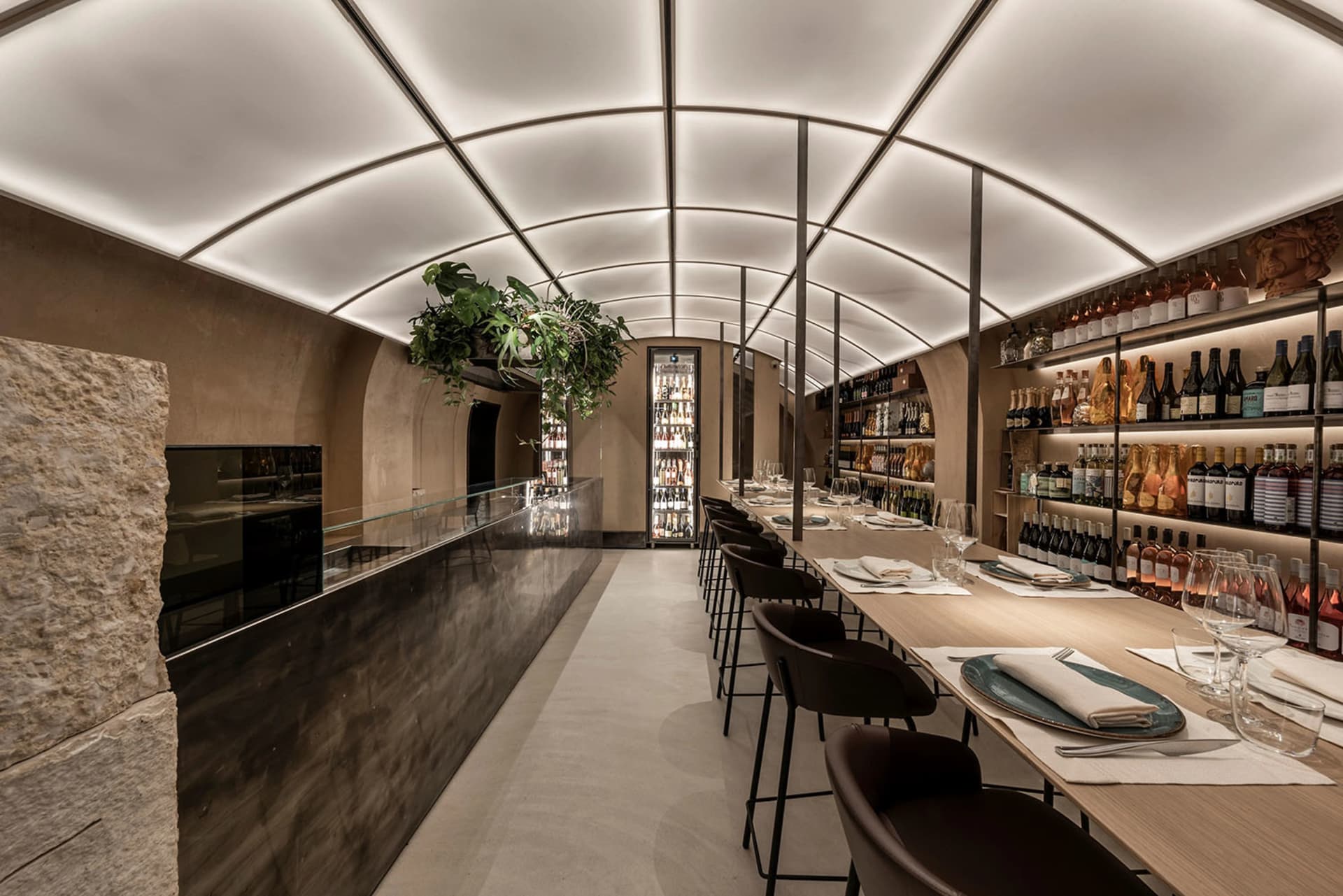 A modern wine bar with concrete countertops, wood shelves, and glass bottles of wine.