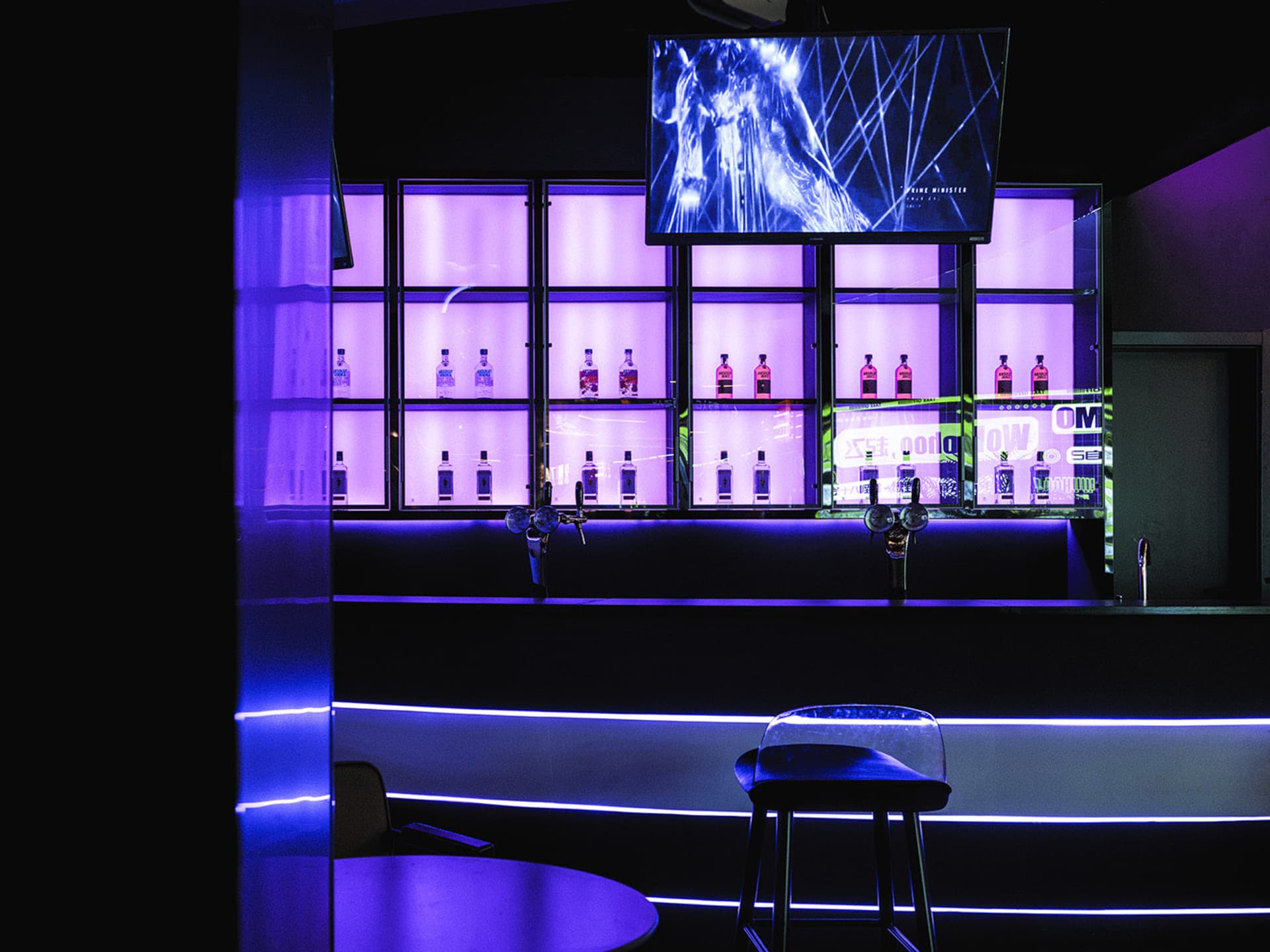 Modern bar interior with purple LED lights and illuminated shelving displaying bottles of alcohol.