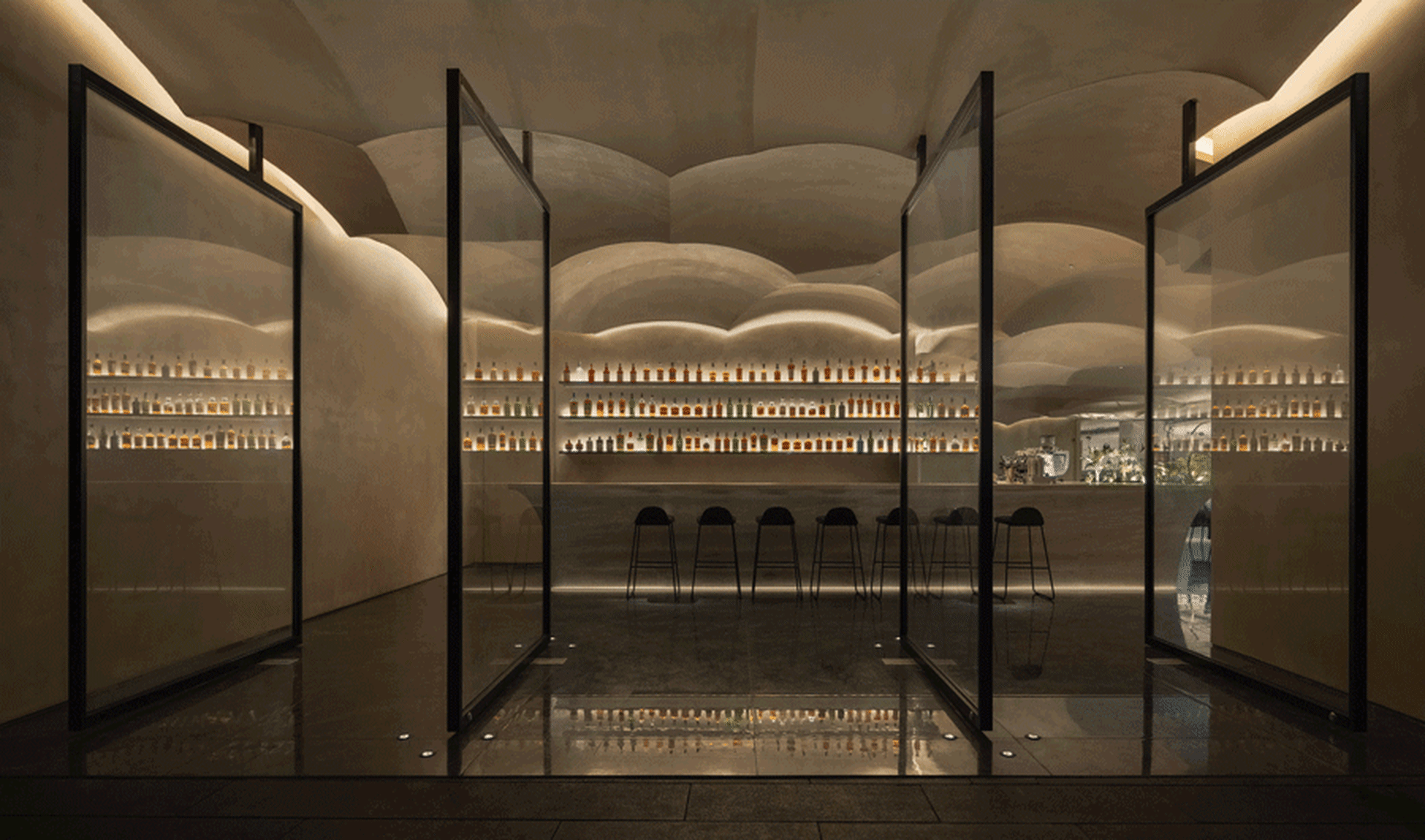 A modern bar with a transparent glass countertop and a collection of bottles in the background.