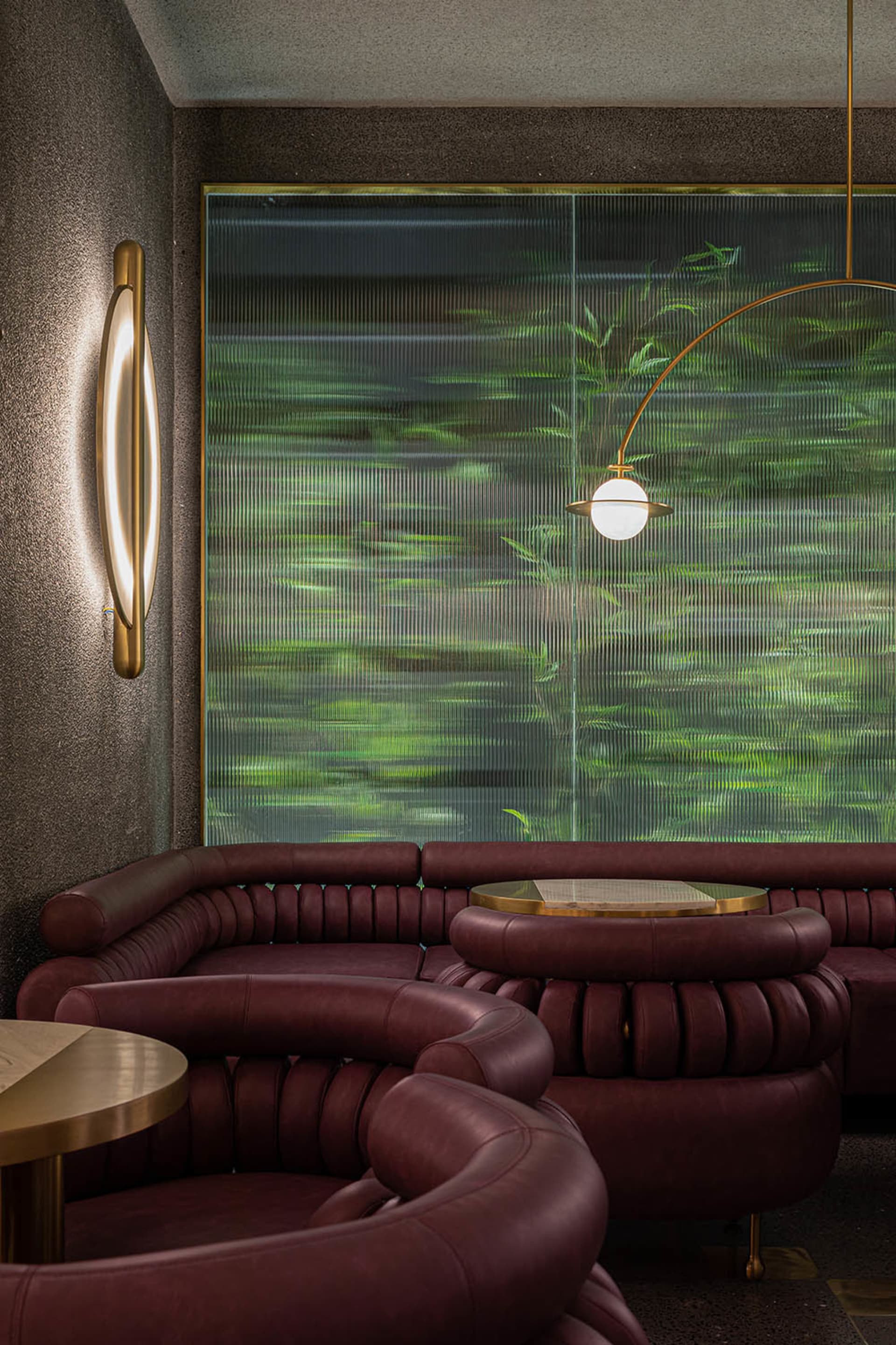 Modern interior design featuring curved leather sofas in front of a large, textured glass window showcasing green foliage.