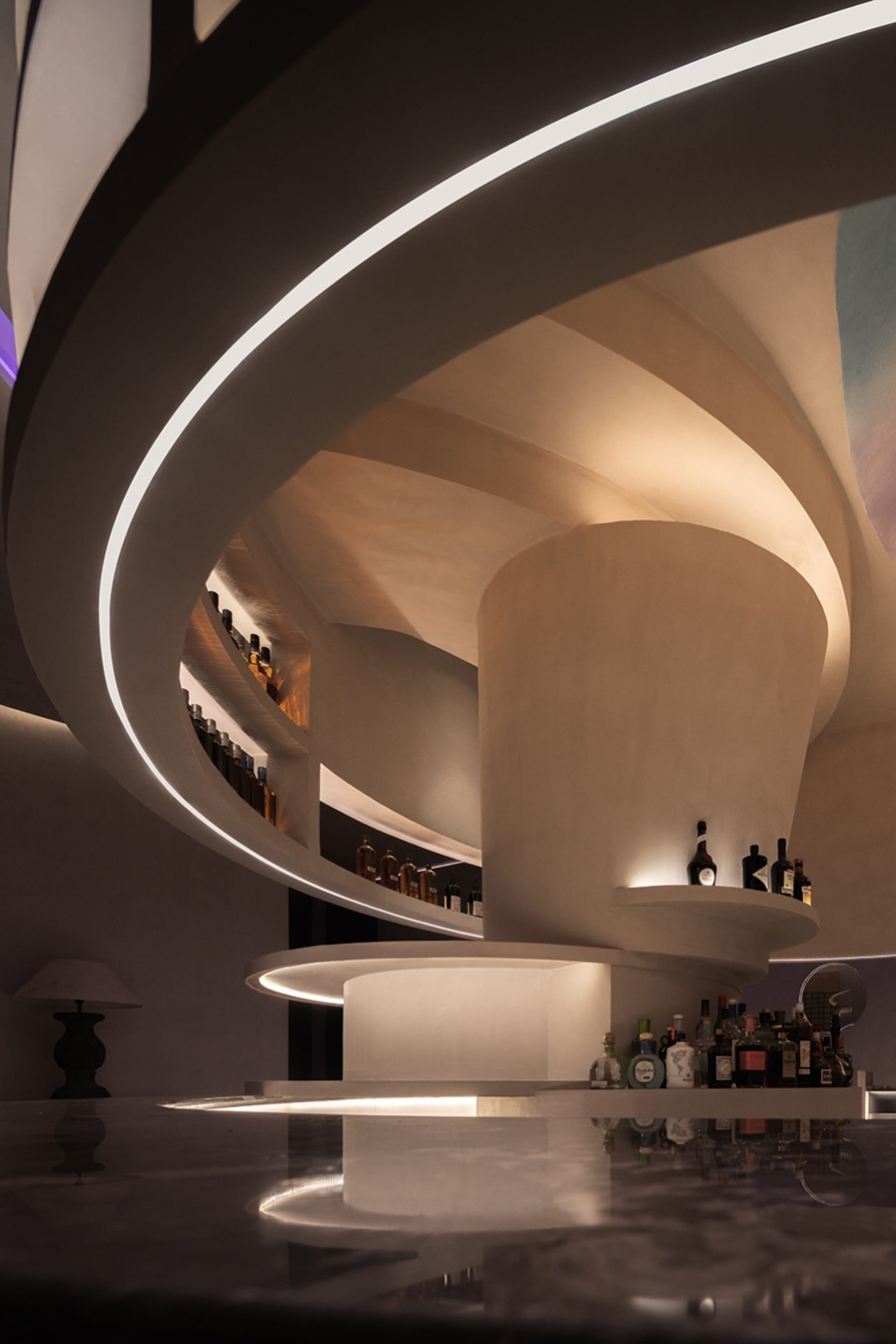 A modern bar interior with concrete elements and illuminated shelves.