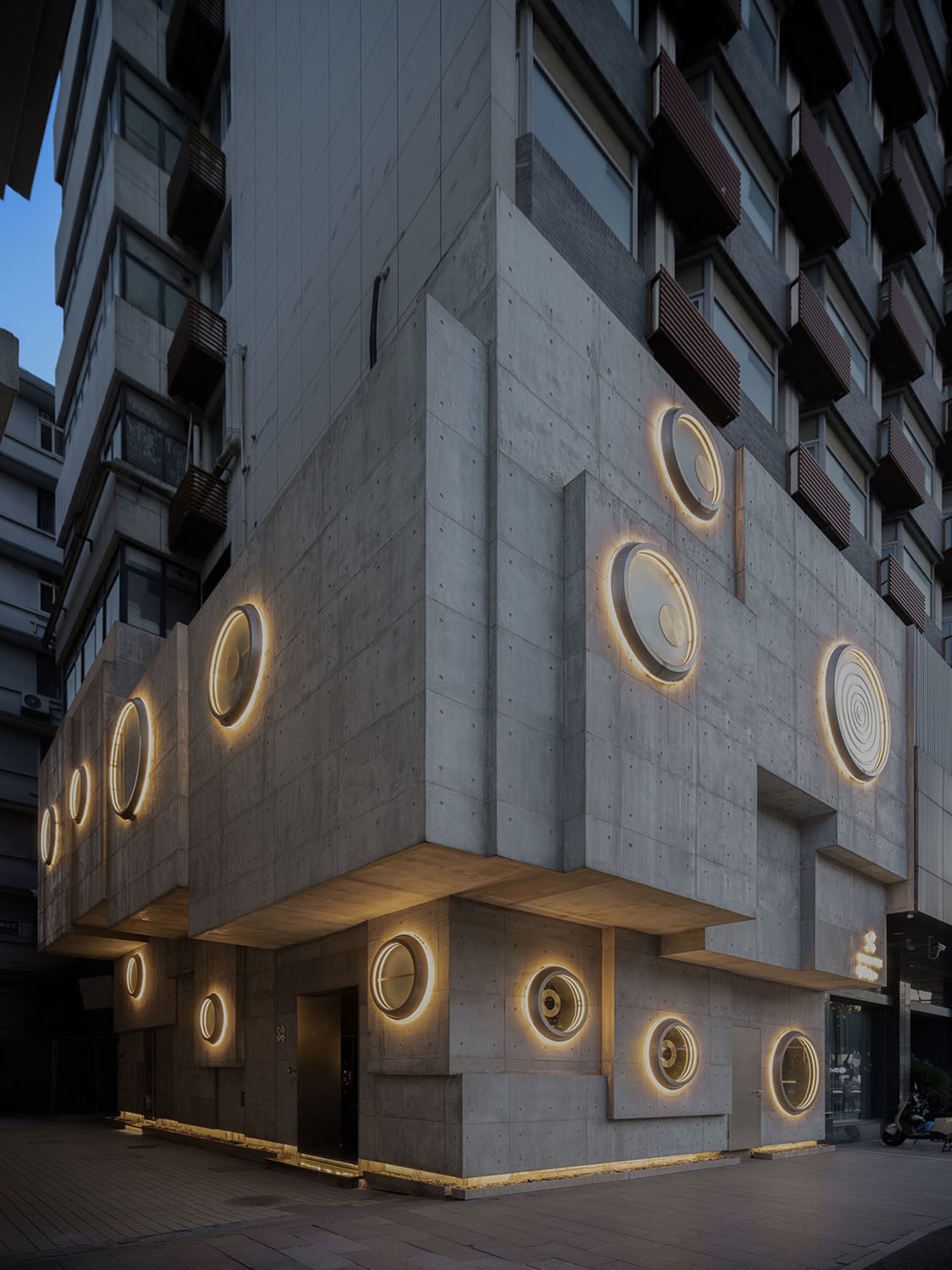 一座混凝土建築的現代店面,搭配圓形窗戶與溫暖的氛圍燈光。