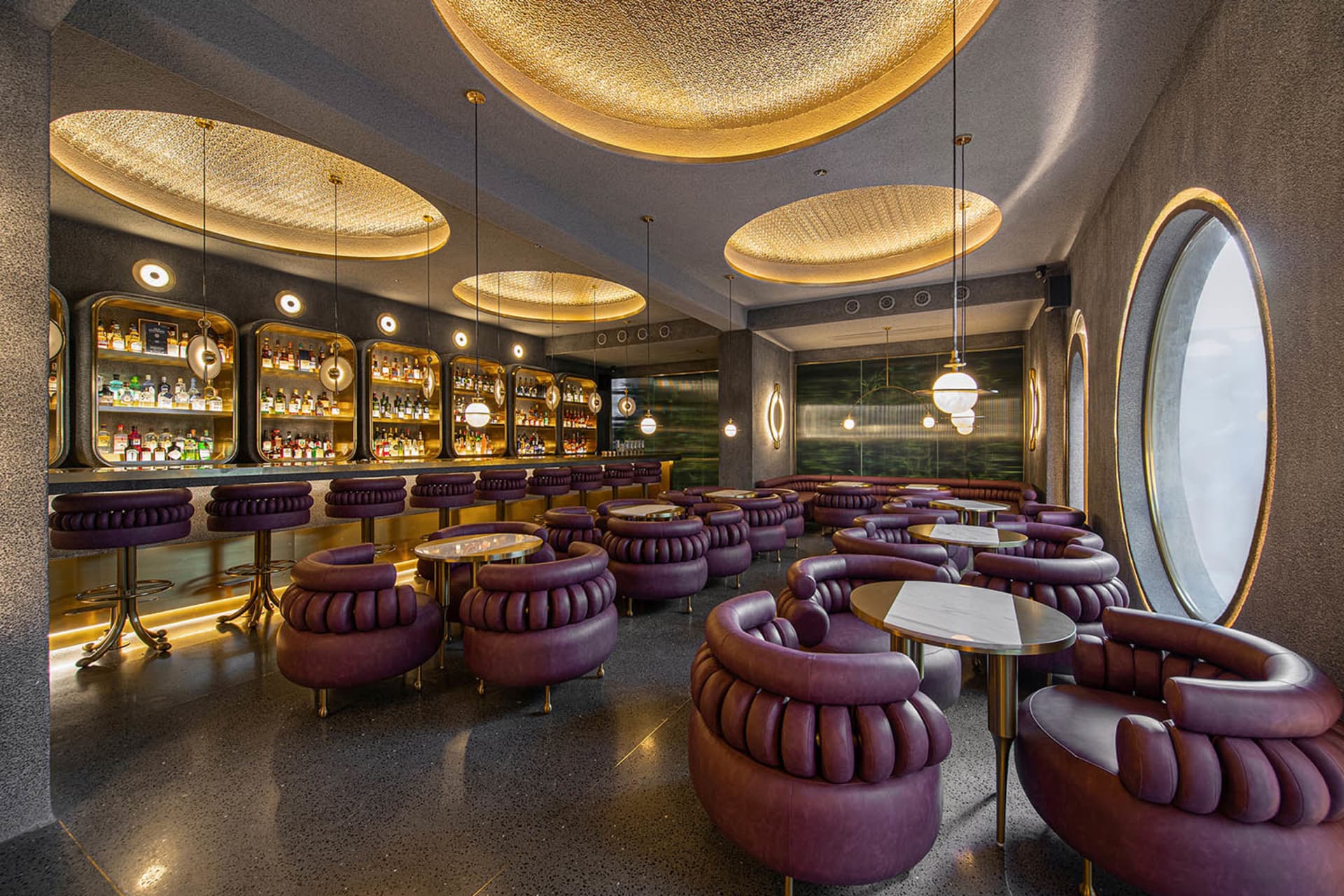 A modern industrial-style hospitality bar with purple leather furniture and circular light fixtures.