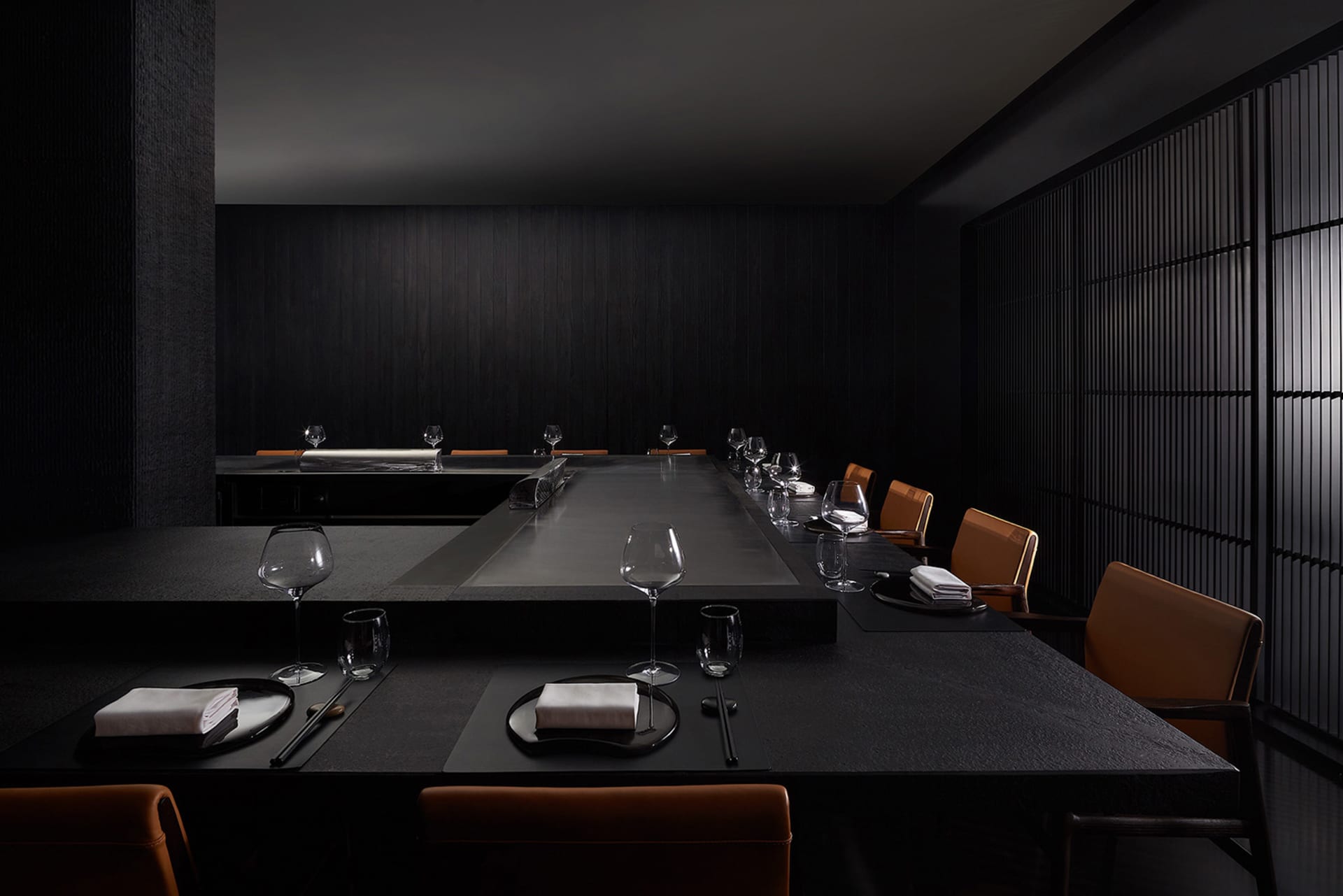 A modern restaurant interior featuring a sleek black stone dining area with minimalist decor and elegant table settings.