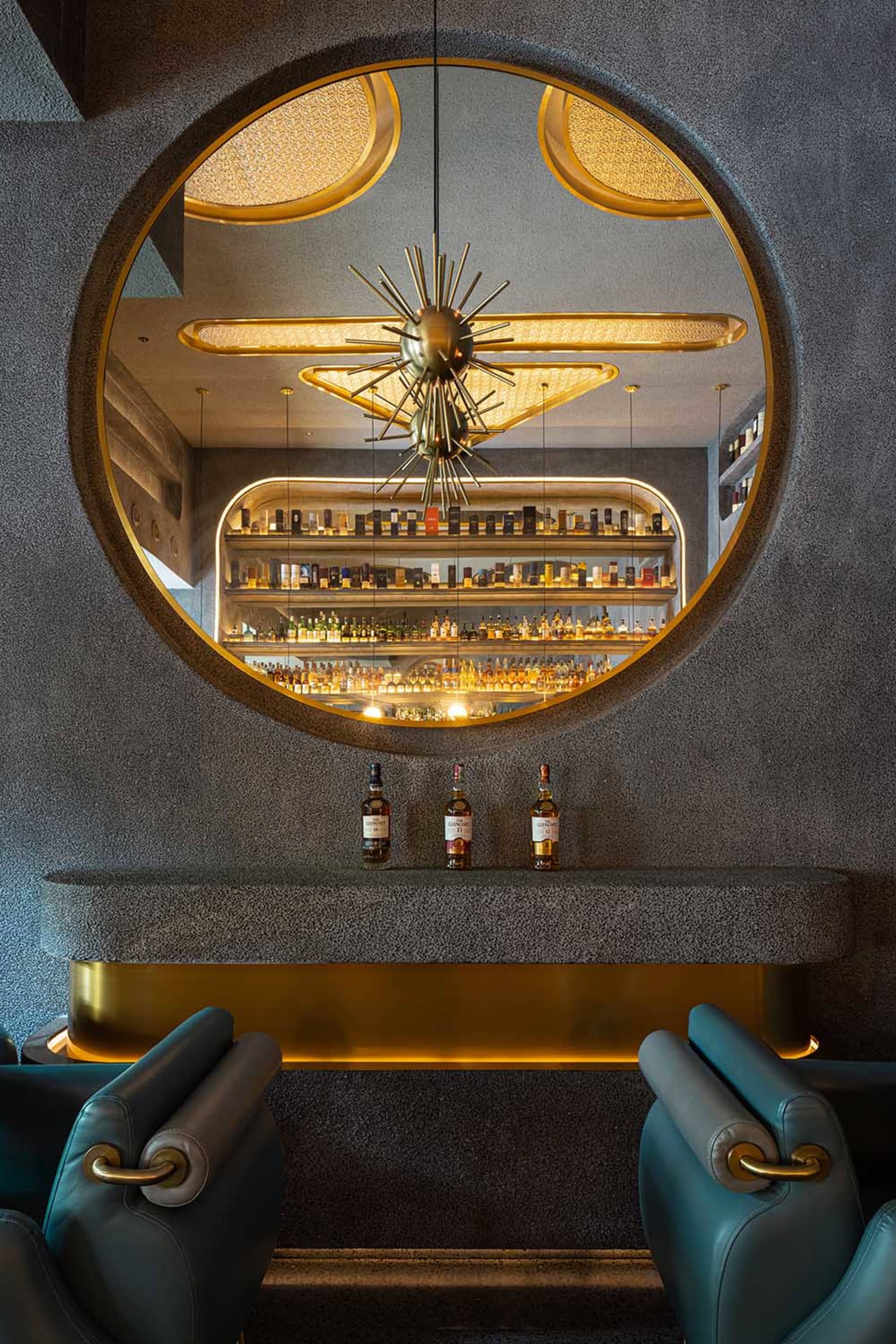 Modern industrial restaurant bar interior with concrete walls, brass accents, and circular window showcasing a well-stocked b