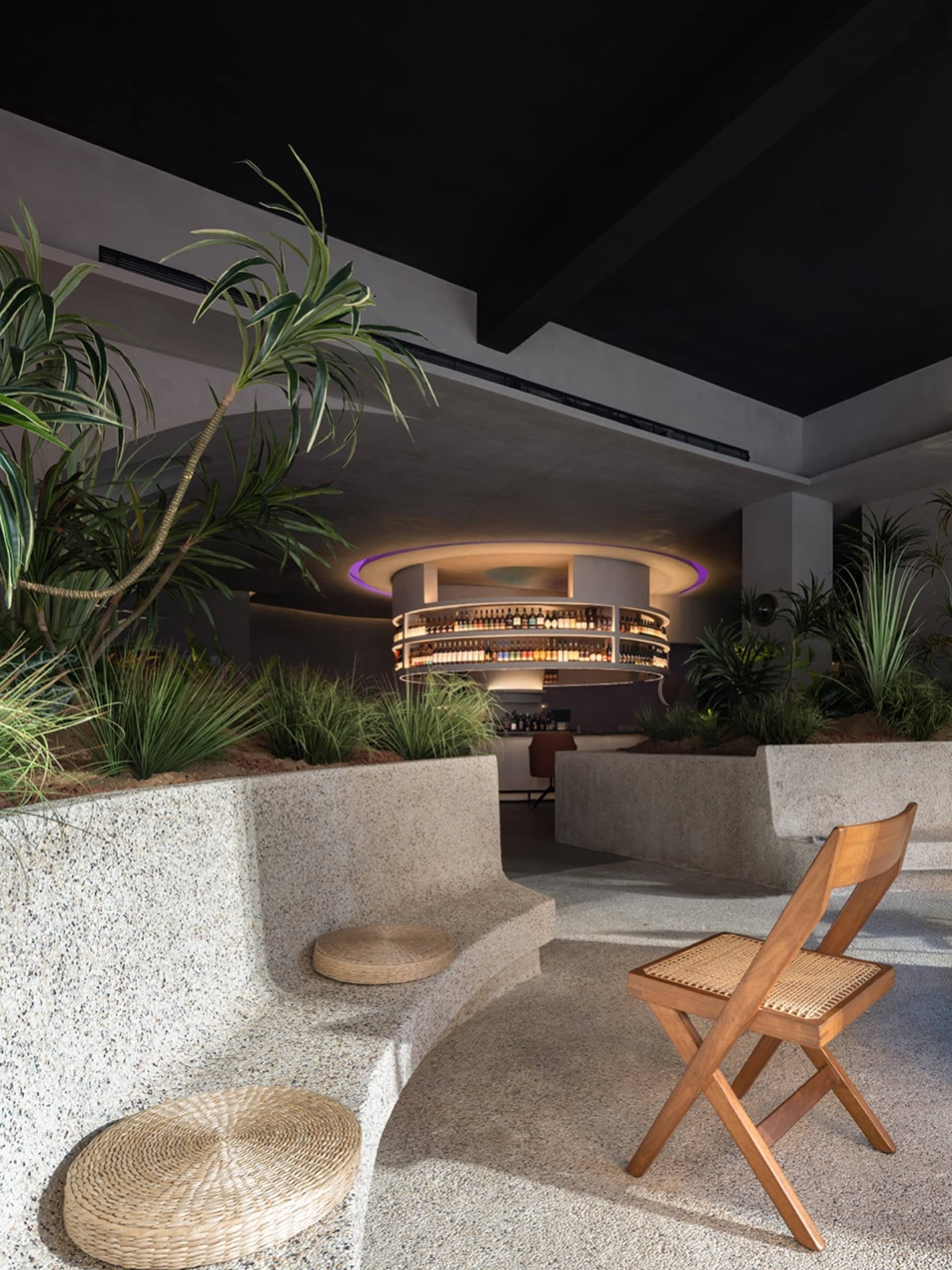 A modern bar interior featuring granite seating, concrete walls, and timber chairs with a circular bar counter in the backgro