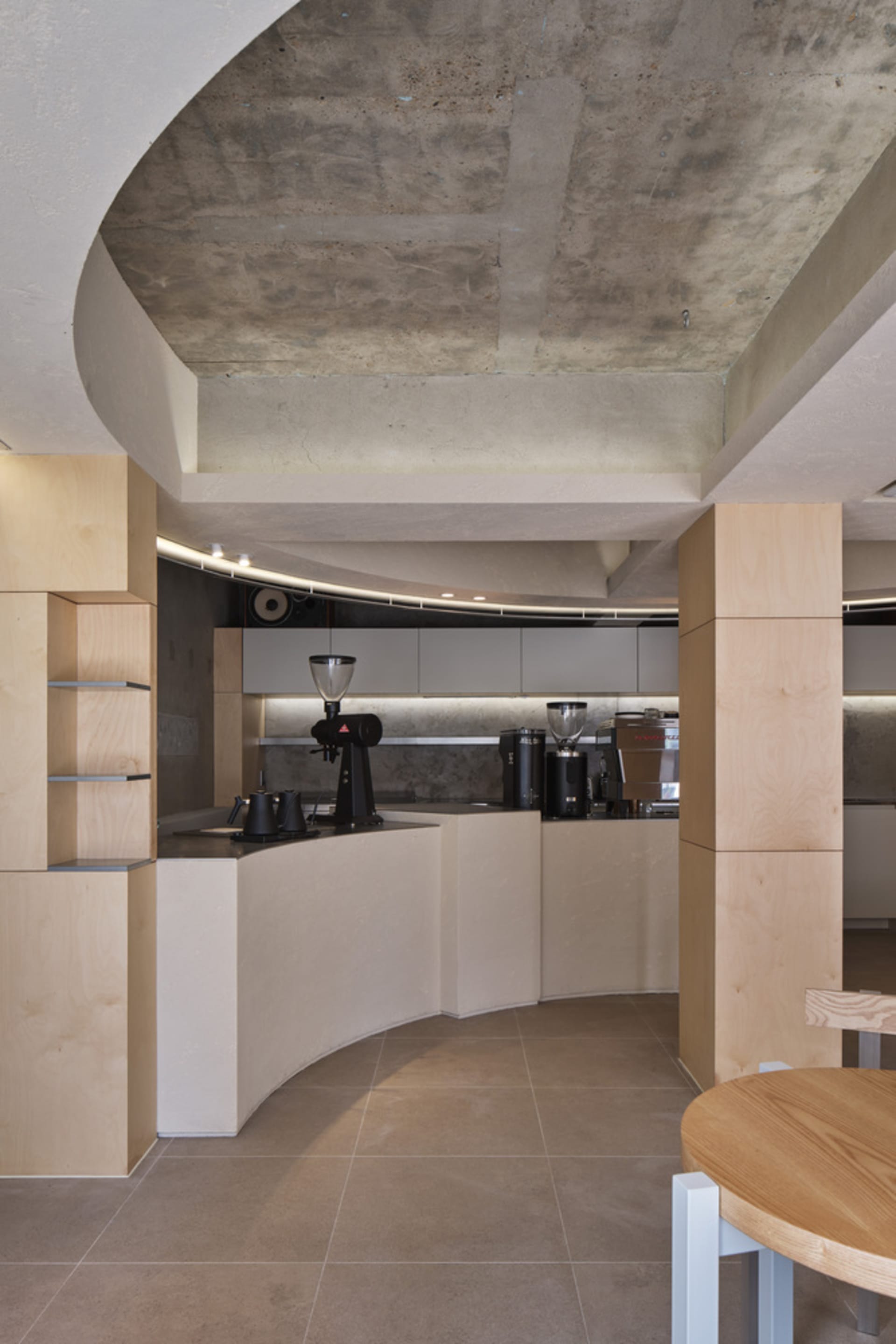 Industrial-style coffee shop kitchen featuring concrete walls, minimalist design, and modern coffee equipment.