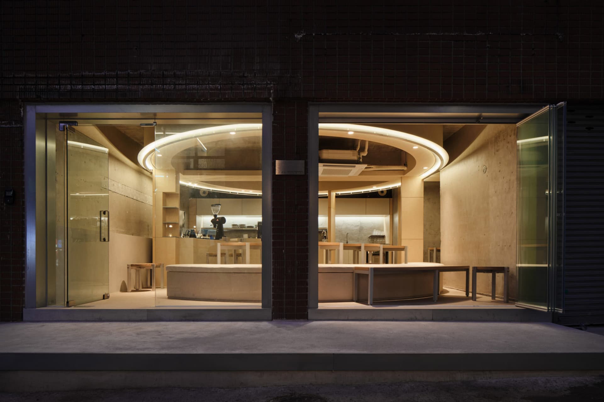 A modern restaurant with concrete and wooden elements, featuring open seating and a bar counter.