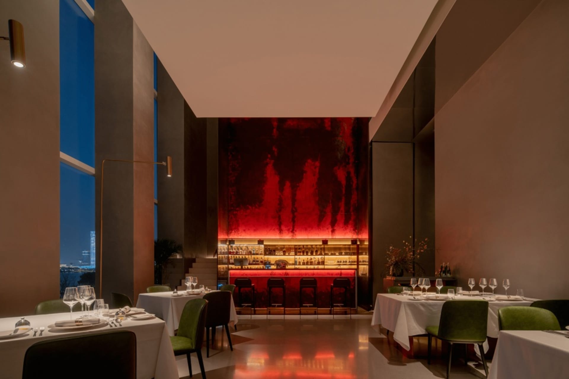 A modern industrial restaurant interior with red lighting and green chairs.