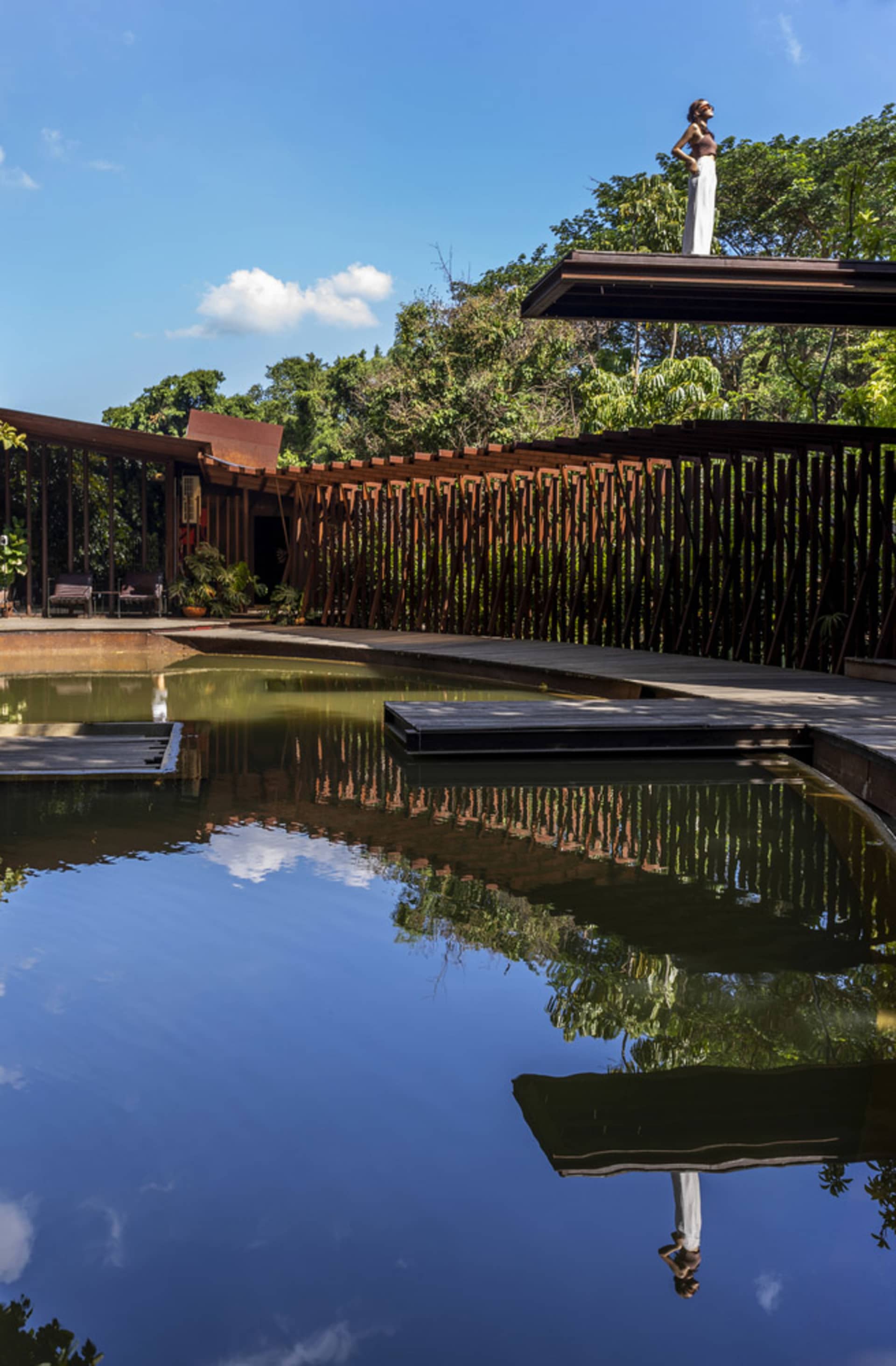 A minimalist pavilion featuring a wooden structure and a tranquil water body in a garden setting.