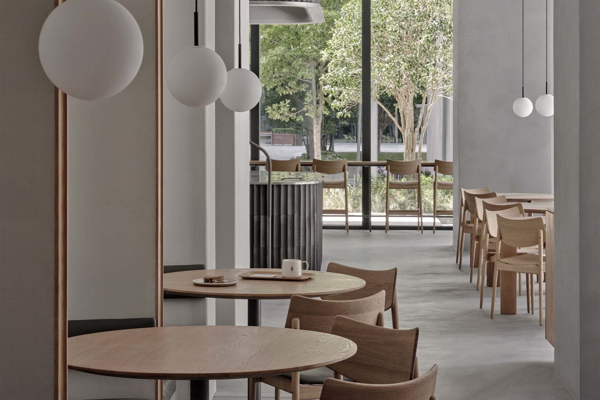 Modern cafe interior covered in wooden furniture, featuring round tables, chairs, and spherical pendant lights.