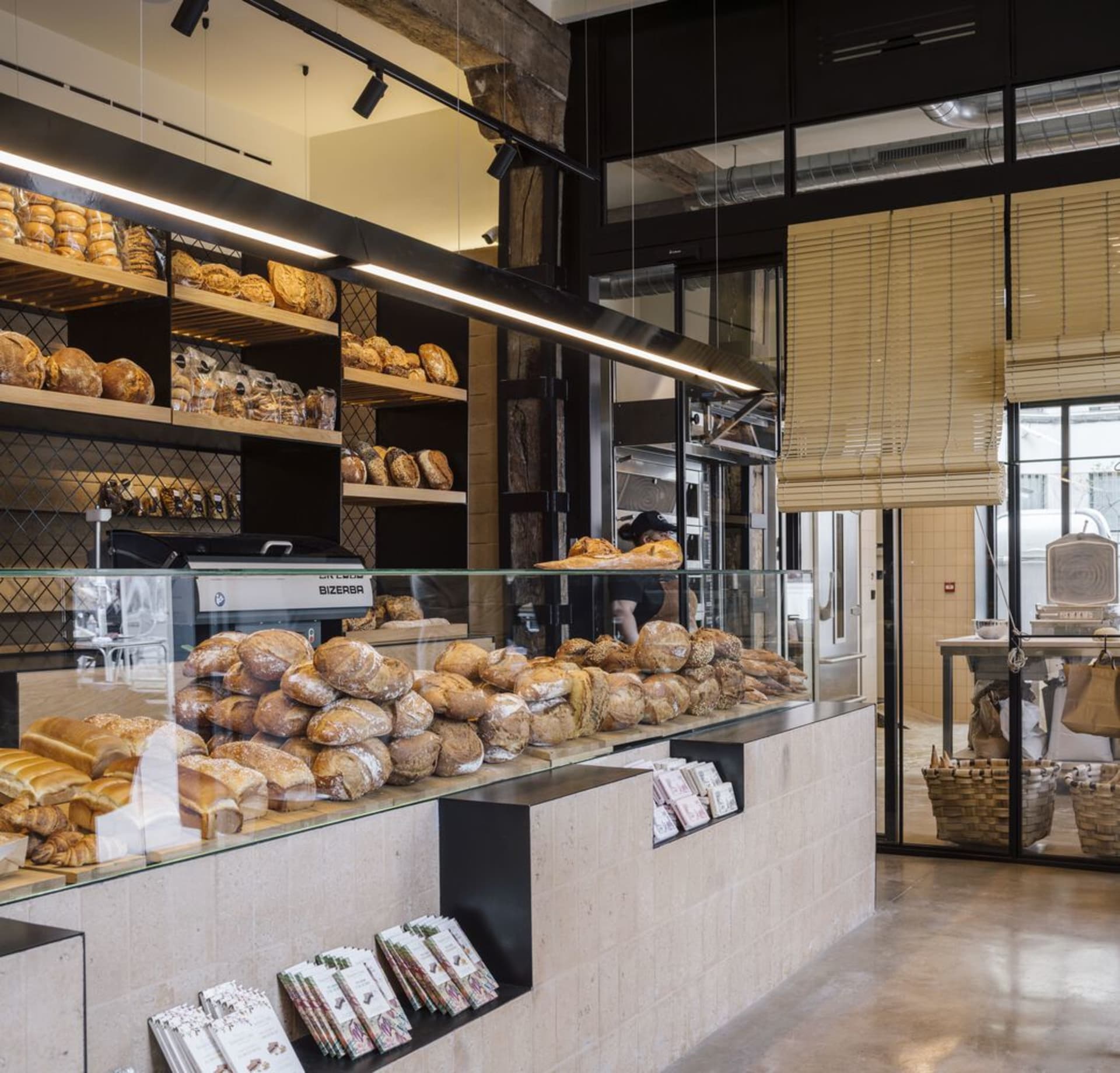 A bakery interior with modern design elements, featuring marble countertops, concrete walls, and wood shelves.
