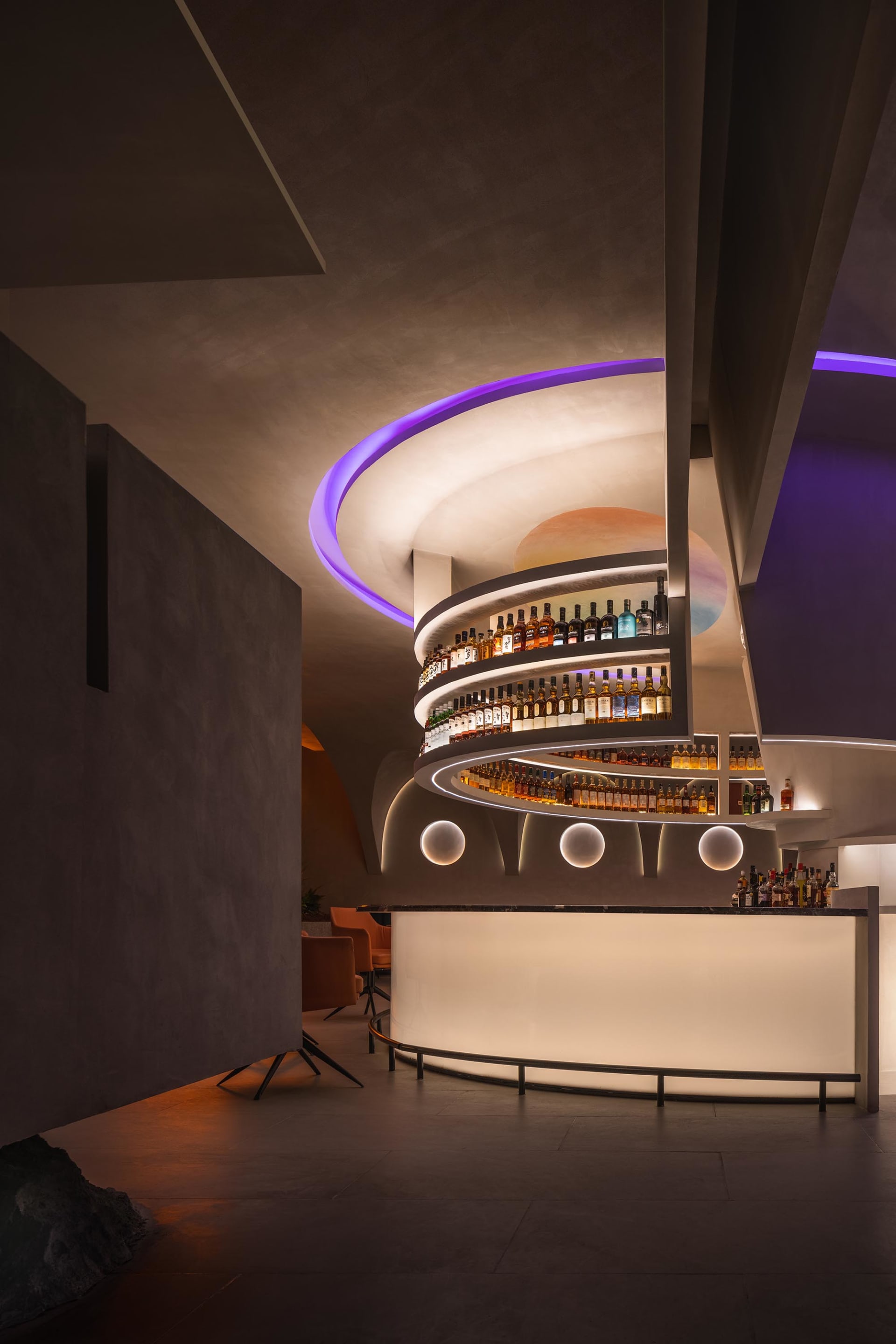 A modern bar with spiral shelves and a concrete wall, featuring a variety of spirits and a warm, ambient light.