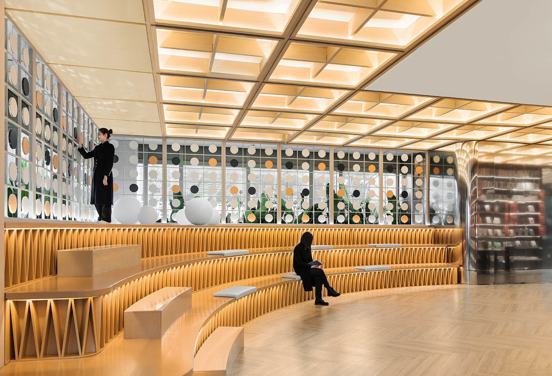 A modern library with a wooden display wall featuring a pattern of circular cutouts.