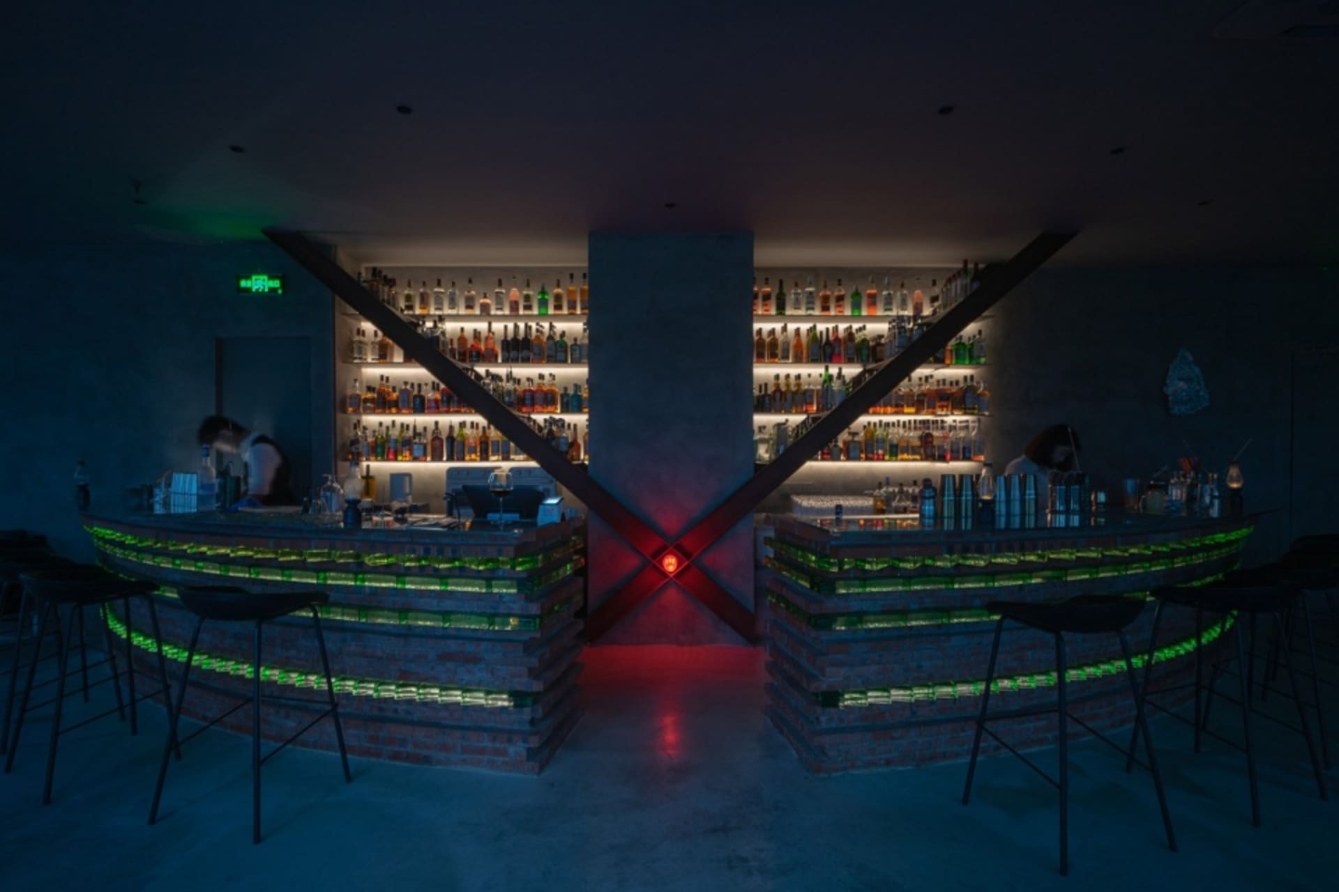 現代酒吧室內，磚面吧台搭配混凝土牆面，由綠色與紅色燈光照亮。