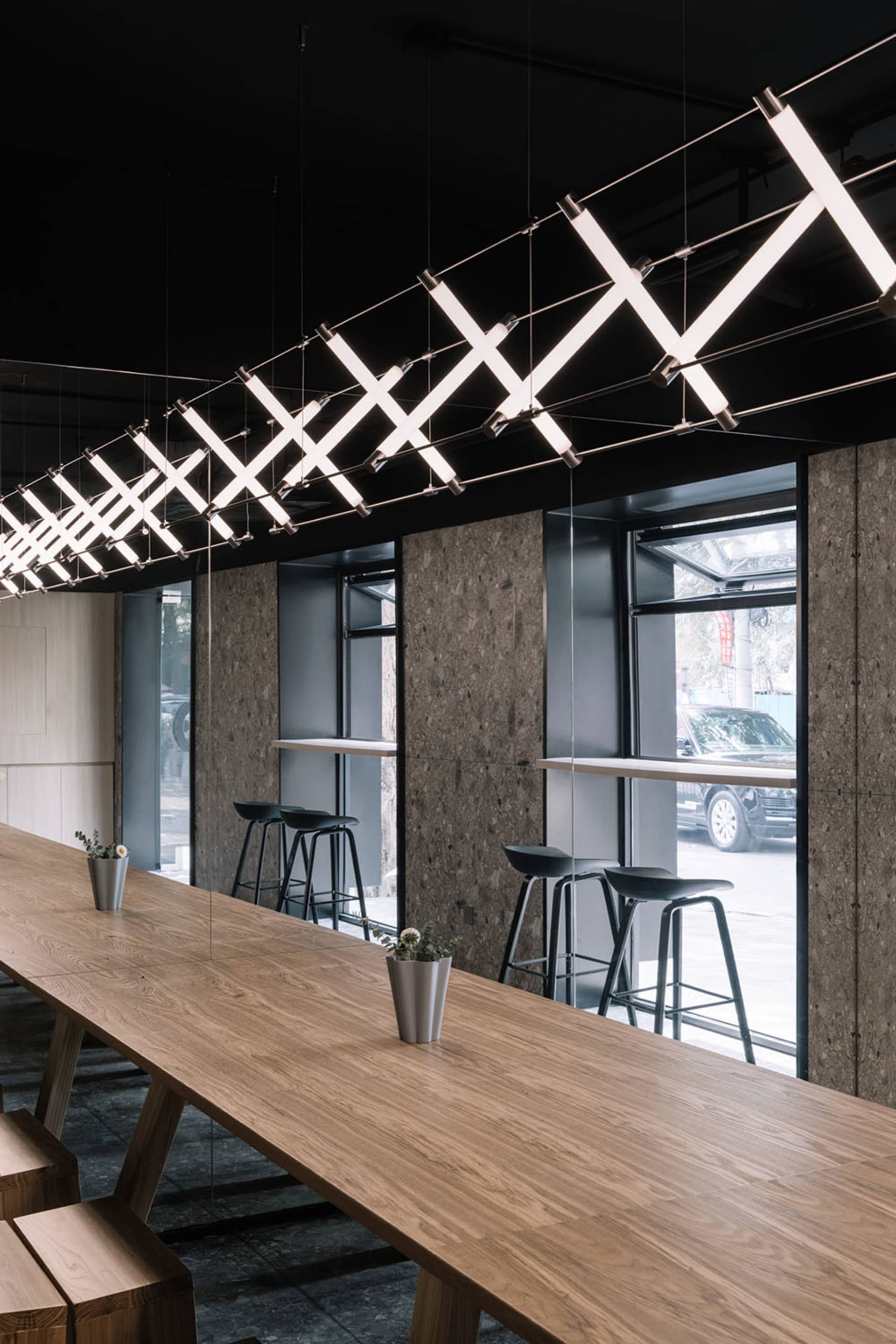 Modern cafe interior with long wooden table, metal stools, and geometric light fixtures