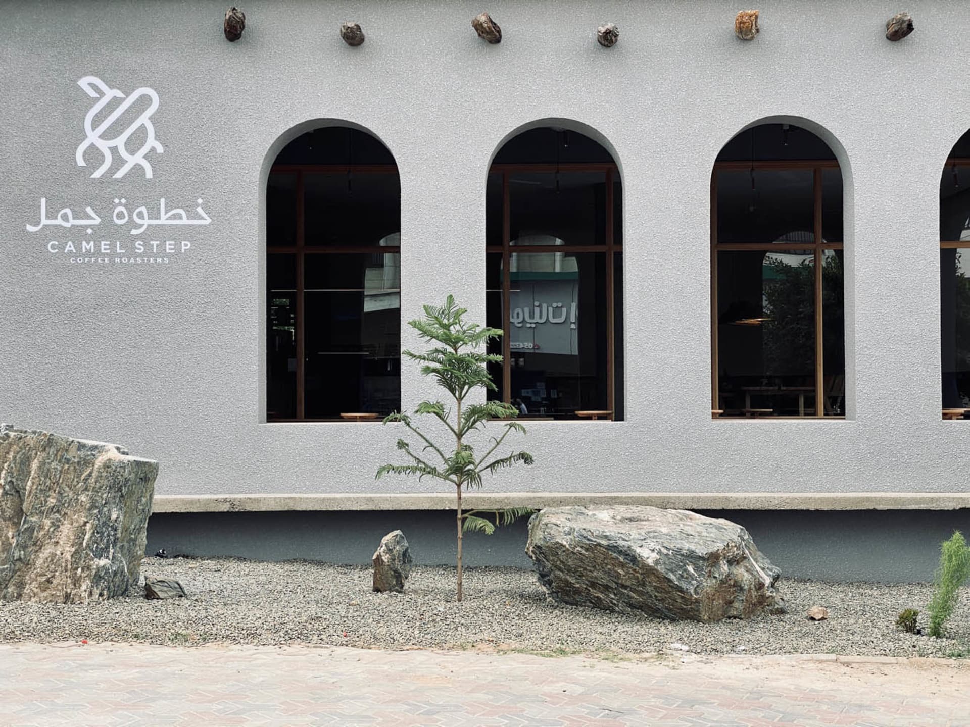 一座現代咖啡店外觀，採用極簡設計，搭配混凝土元素與大型拱形窗。
