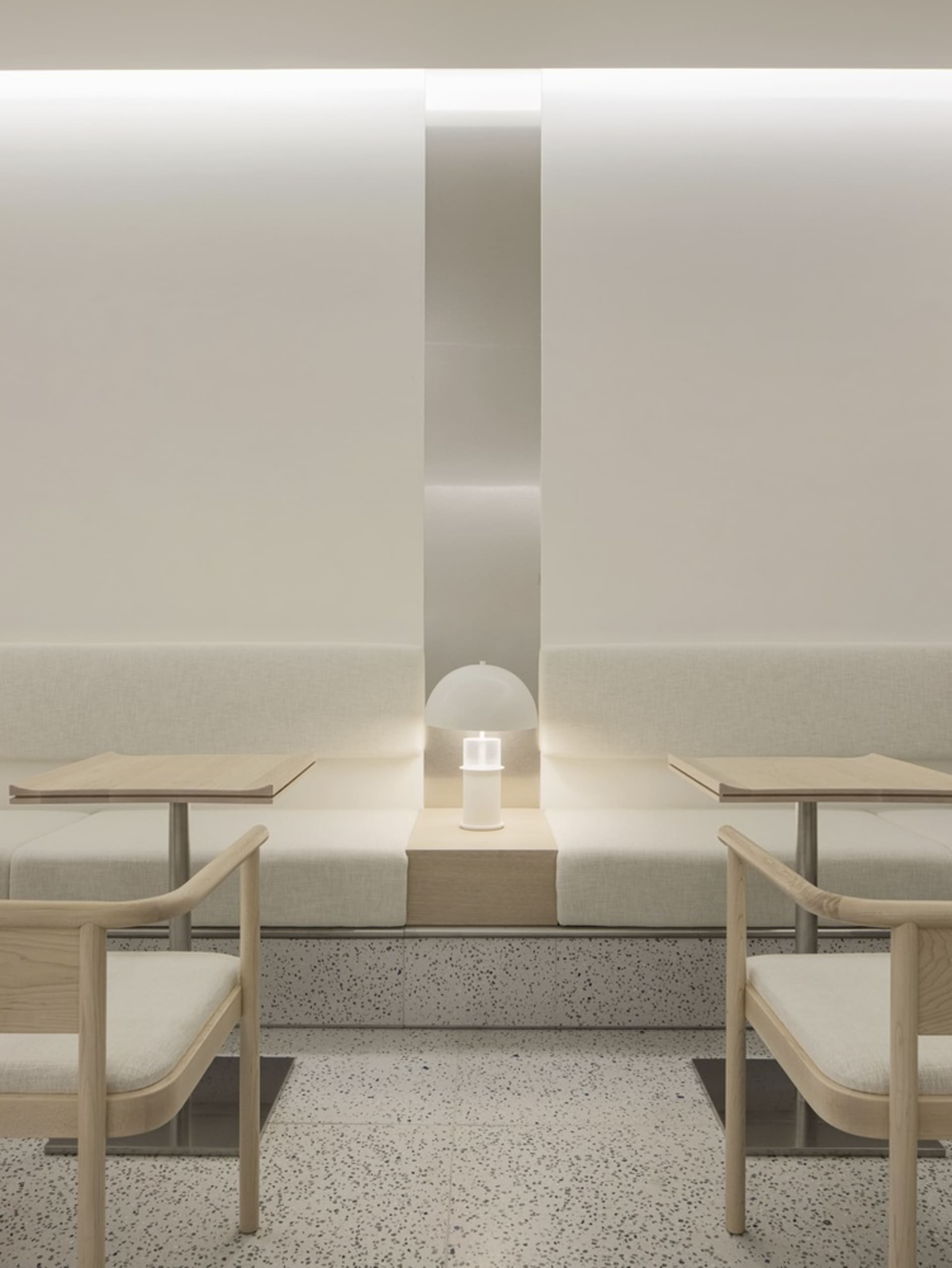 A minimalist restaurant interior with concrete and terrazzo surfaces and a blank white wall.