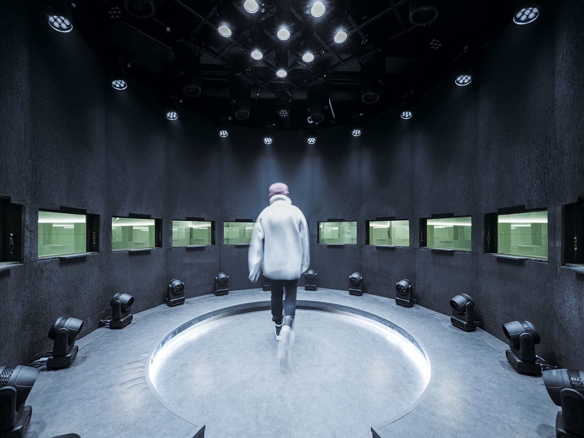 A modern, light-dark room with concrete flooring and walls, featuring a circular centerpiece and multiple lights.