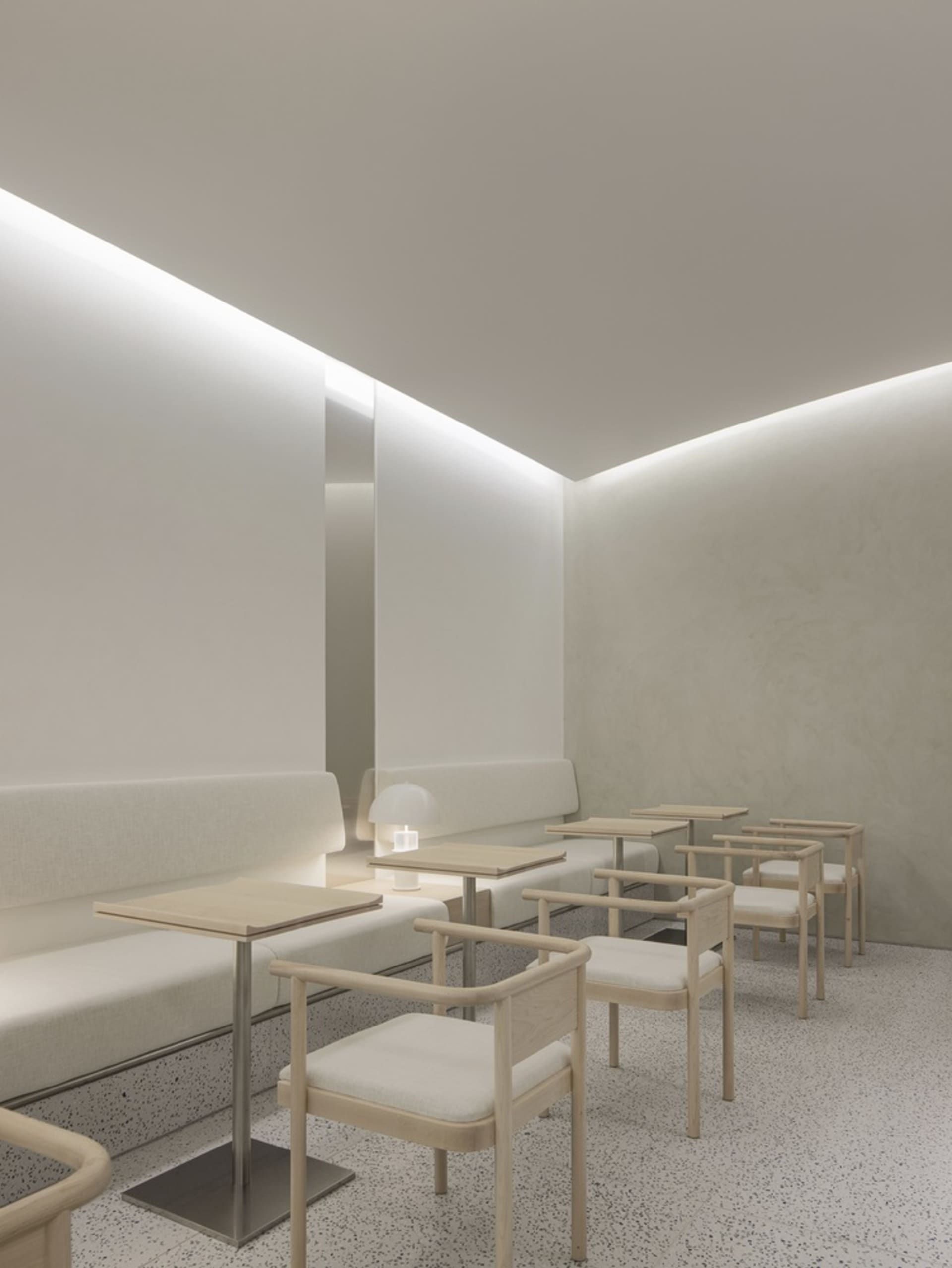 White-themed restaurant interior with minimalist design, wooden chairs, and fabric seating.