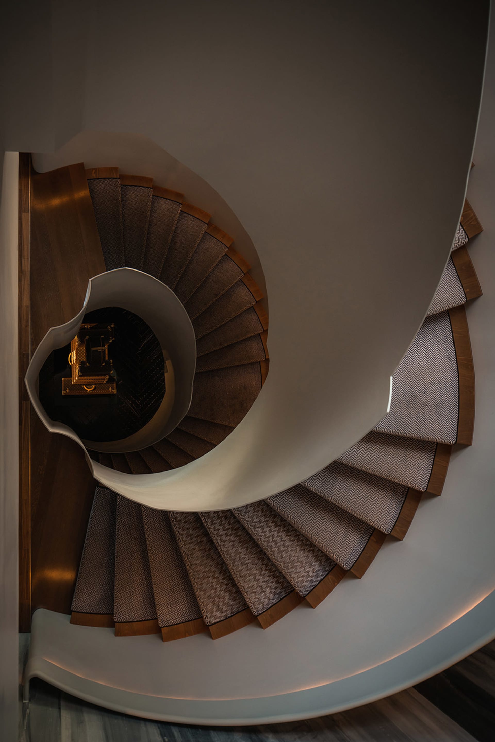 A spiral staircase with carpeted steps viewed from above, highlighting the intricate design and the contrast between the wood