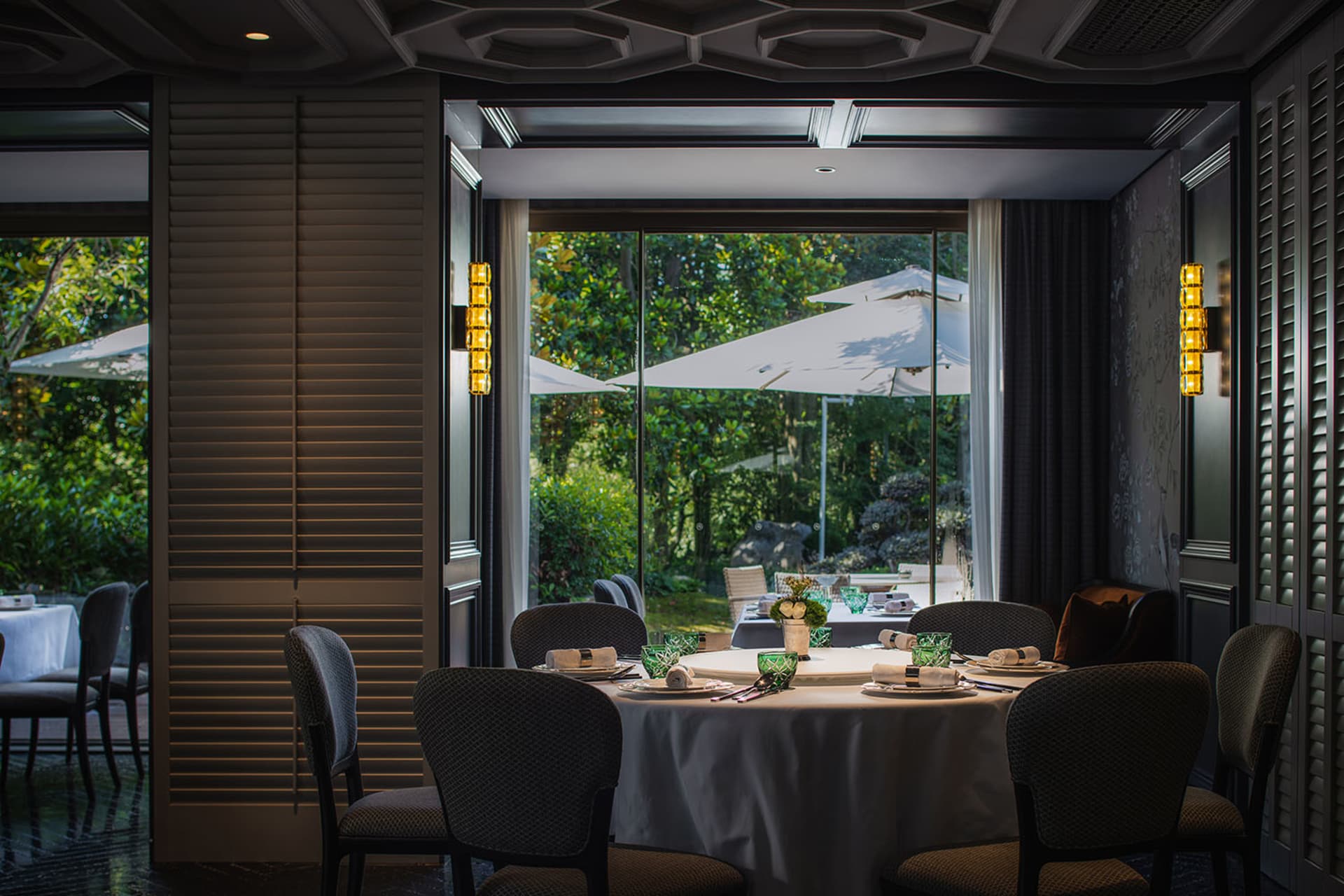 A modern industrial restaurant interior featuring wooden furniture, glass panels, and fabric-covered seating.