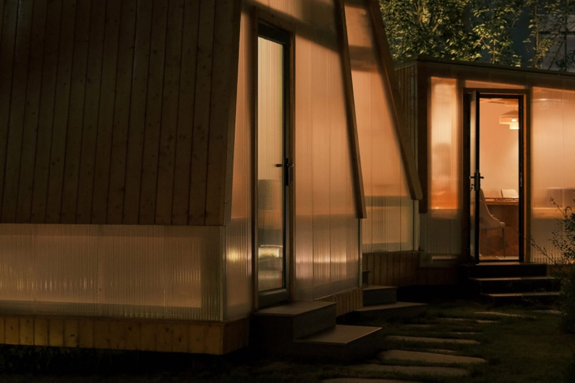 Wood panel clad exterior with glass wall and concrete accents of a minimalist residential home during nighttime with warm ind