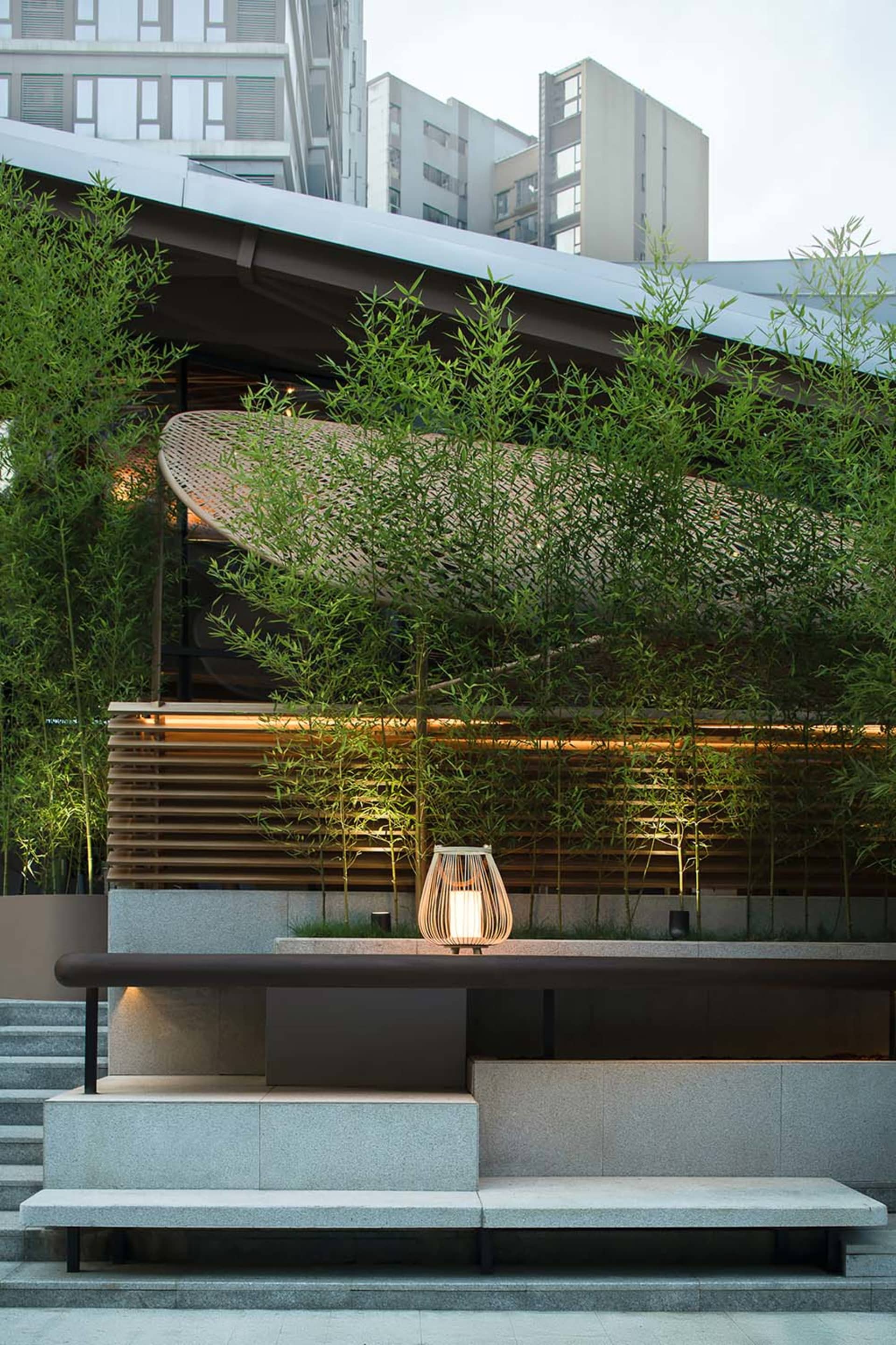 A serene modern-industrial garden with bamboo, lights, and concrete fixtures.