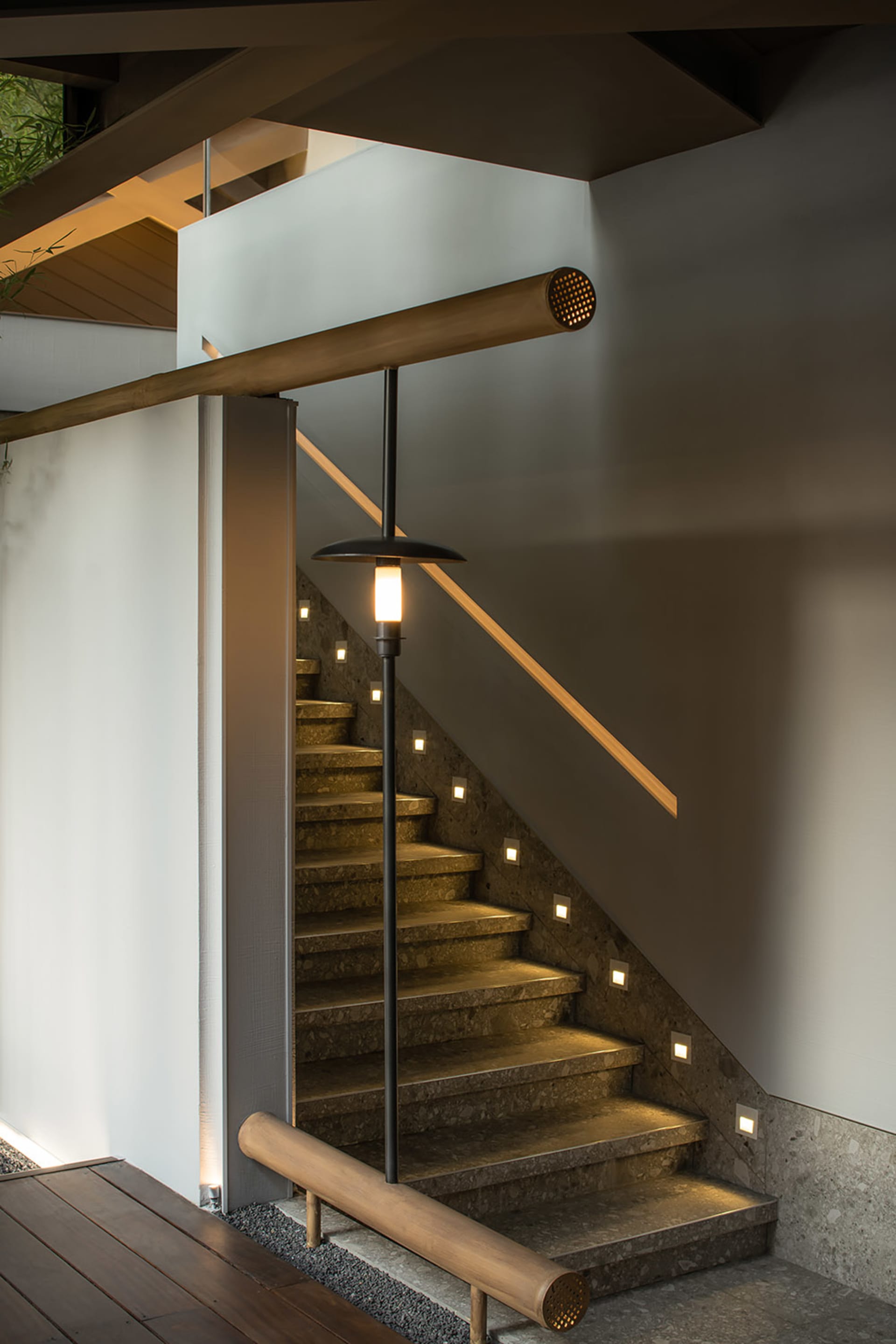A modern interior featuring a concrete staircase with recessed lighting and a wooden handrail.