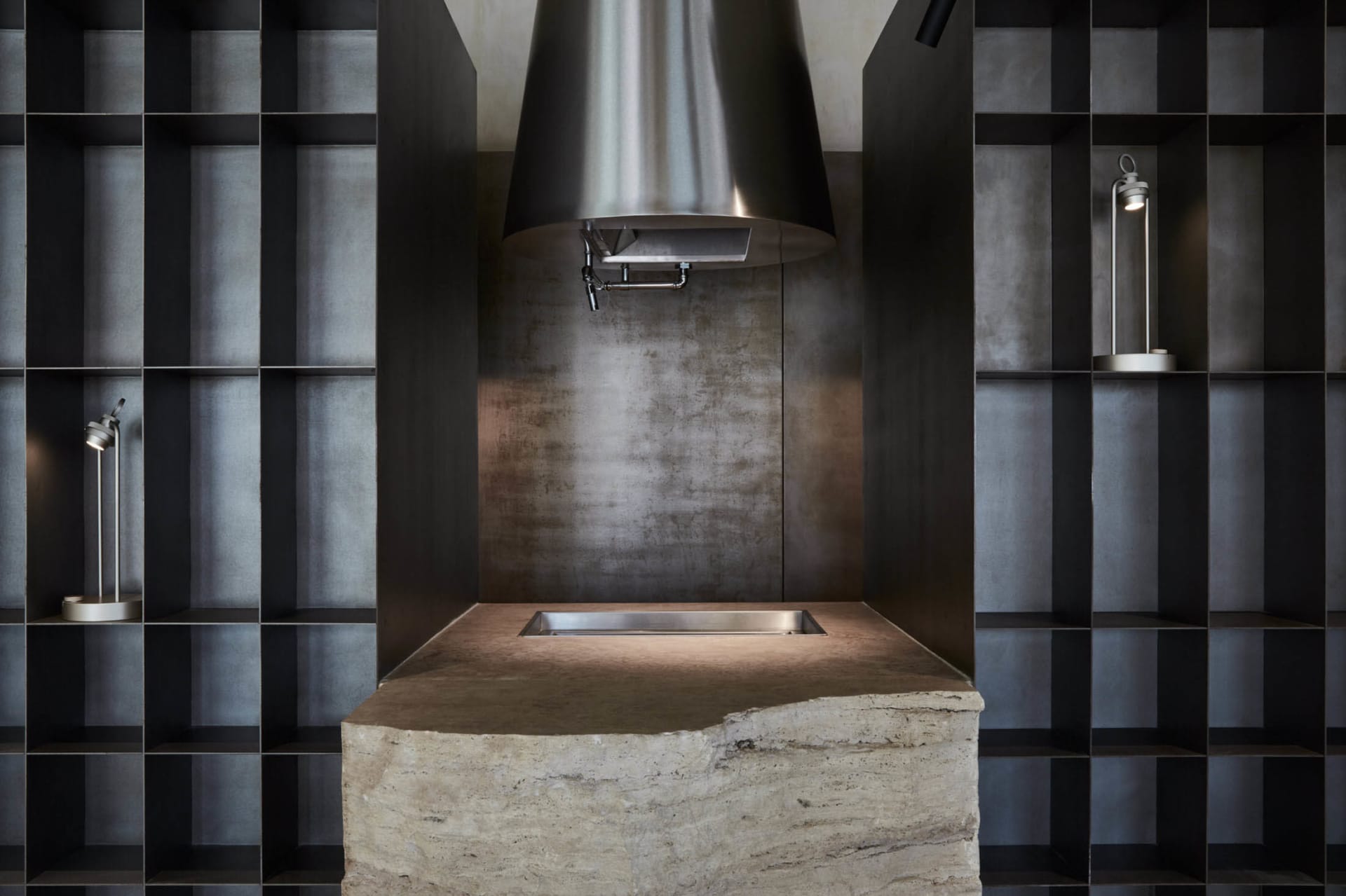A modern industrial kitchen with a concrete countertop and a large stainless steel range hood.