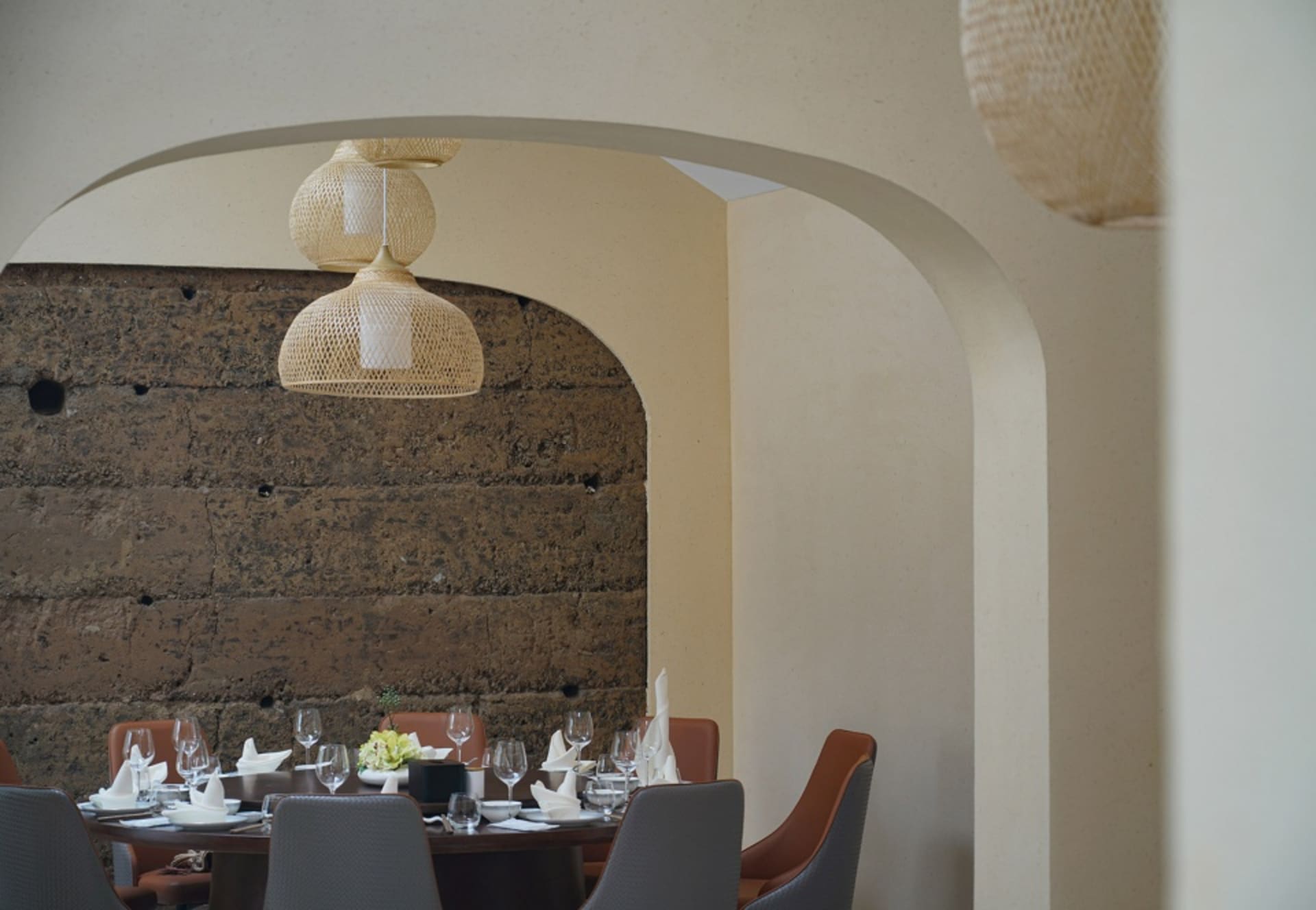 Dining table set with wine glasses and tableware, under woven wood pendant lights in a restaurant interior.