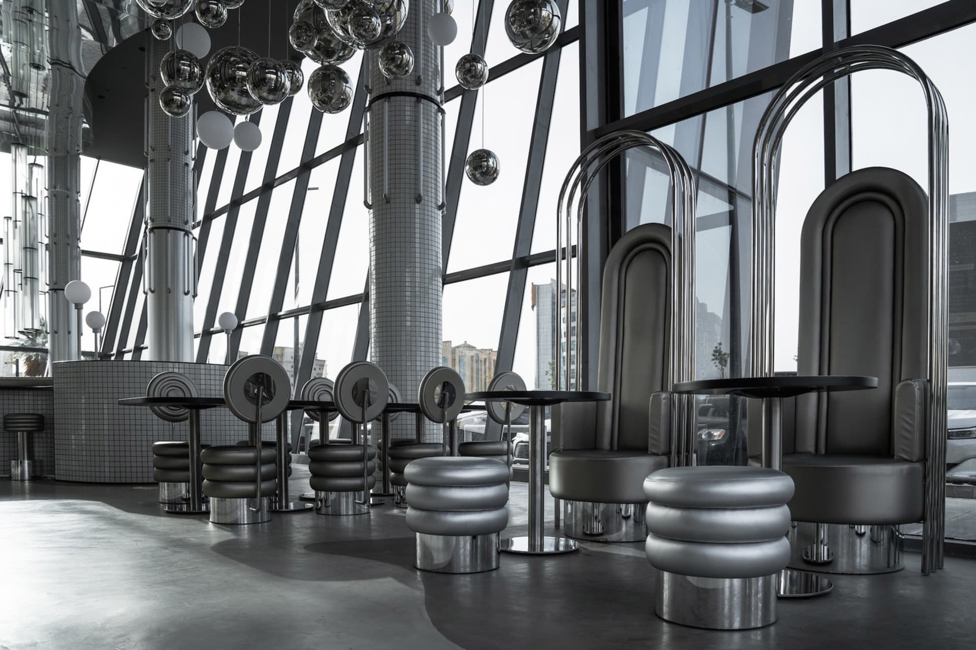 A modern restaurant interior with metallic tables and stools under hanging spherical lights, glass partition seating, and lar