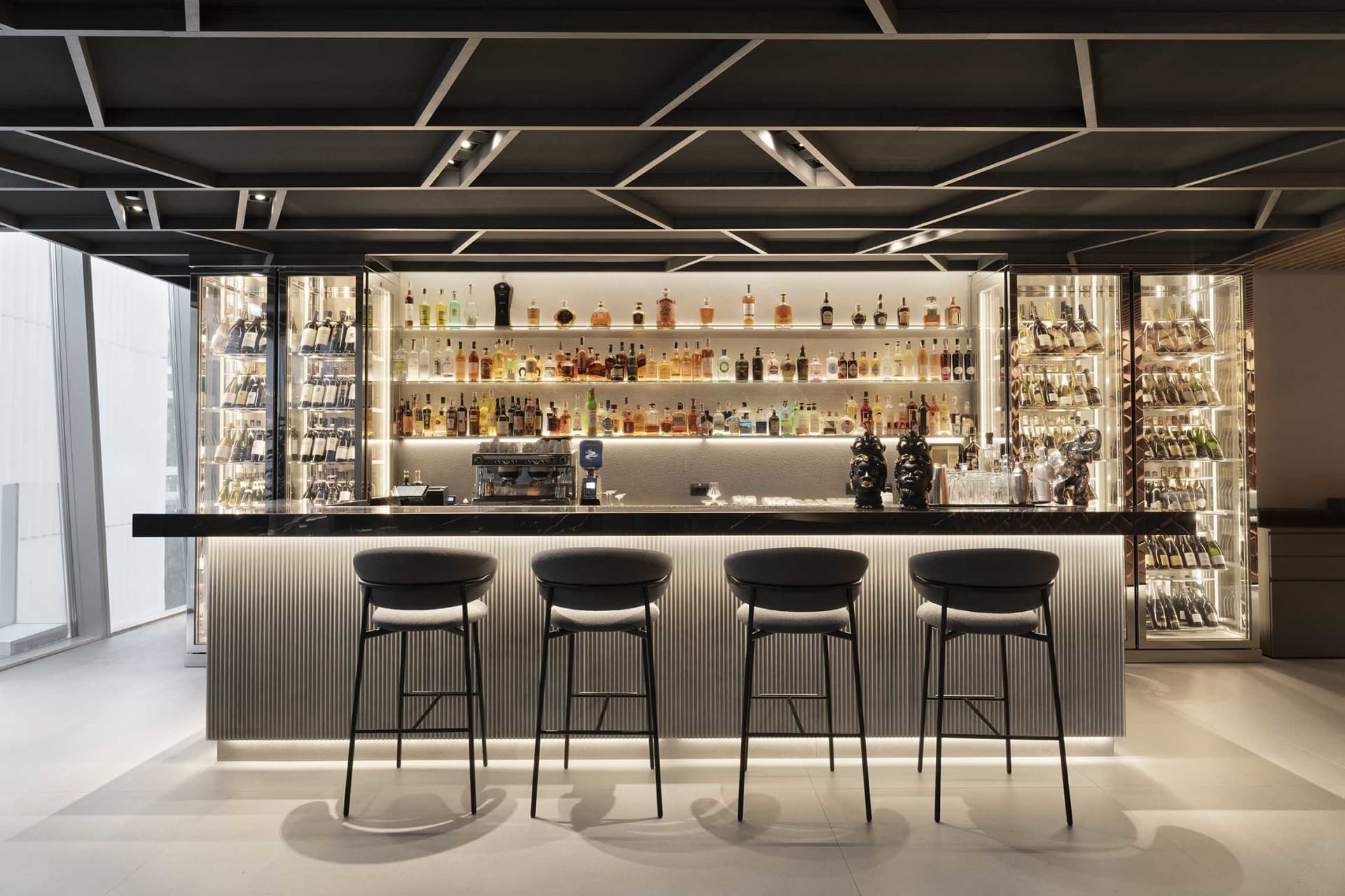A sleek modern bar featuring glass shelves and metal stools.