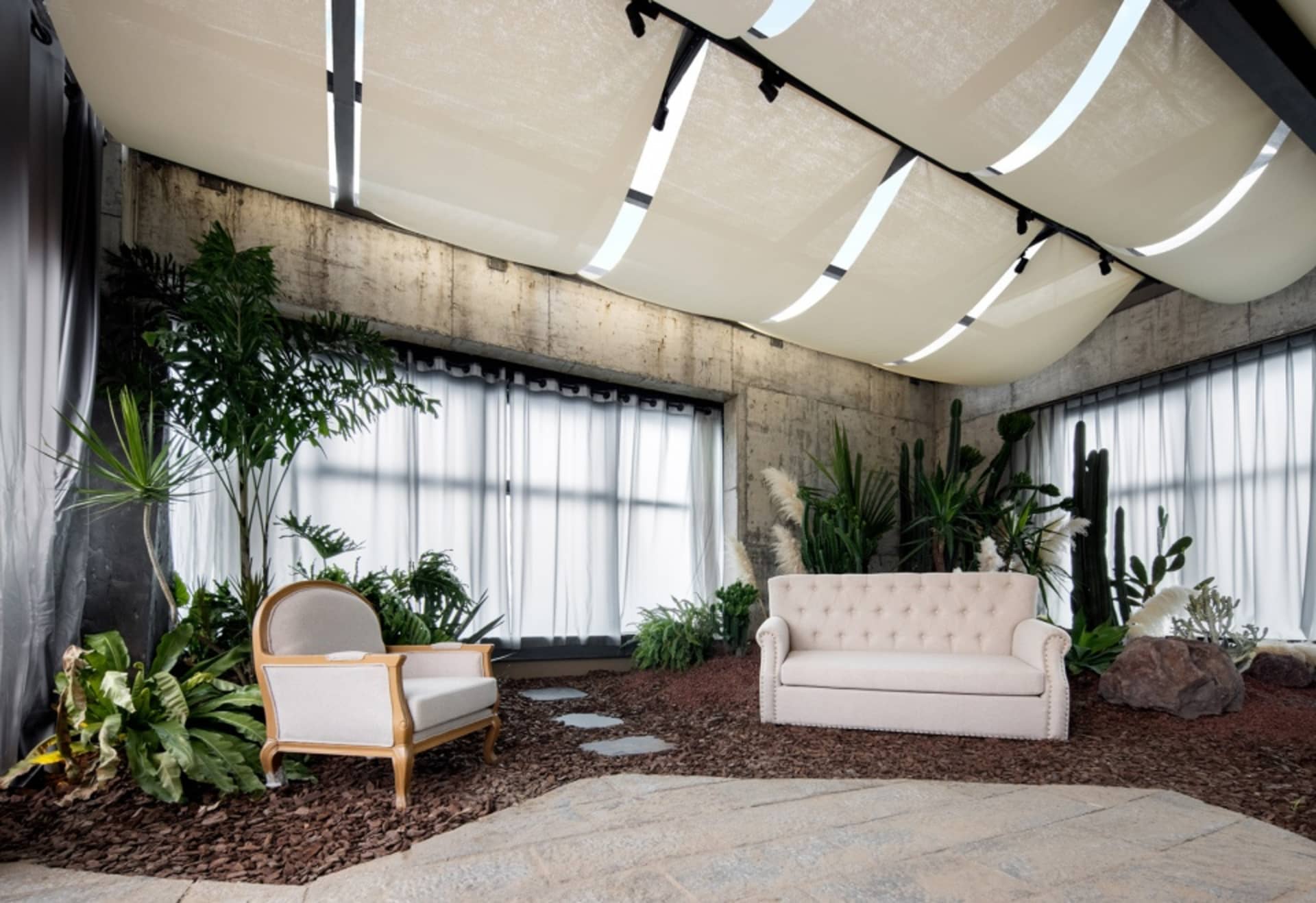 Modern industrial living room featuring concrete walls and ceiling, large windows, and lush greenery.