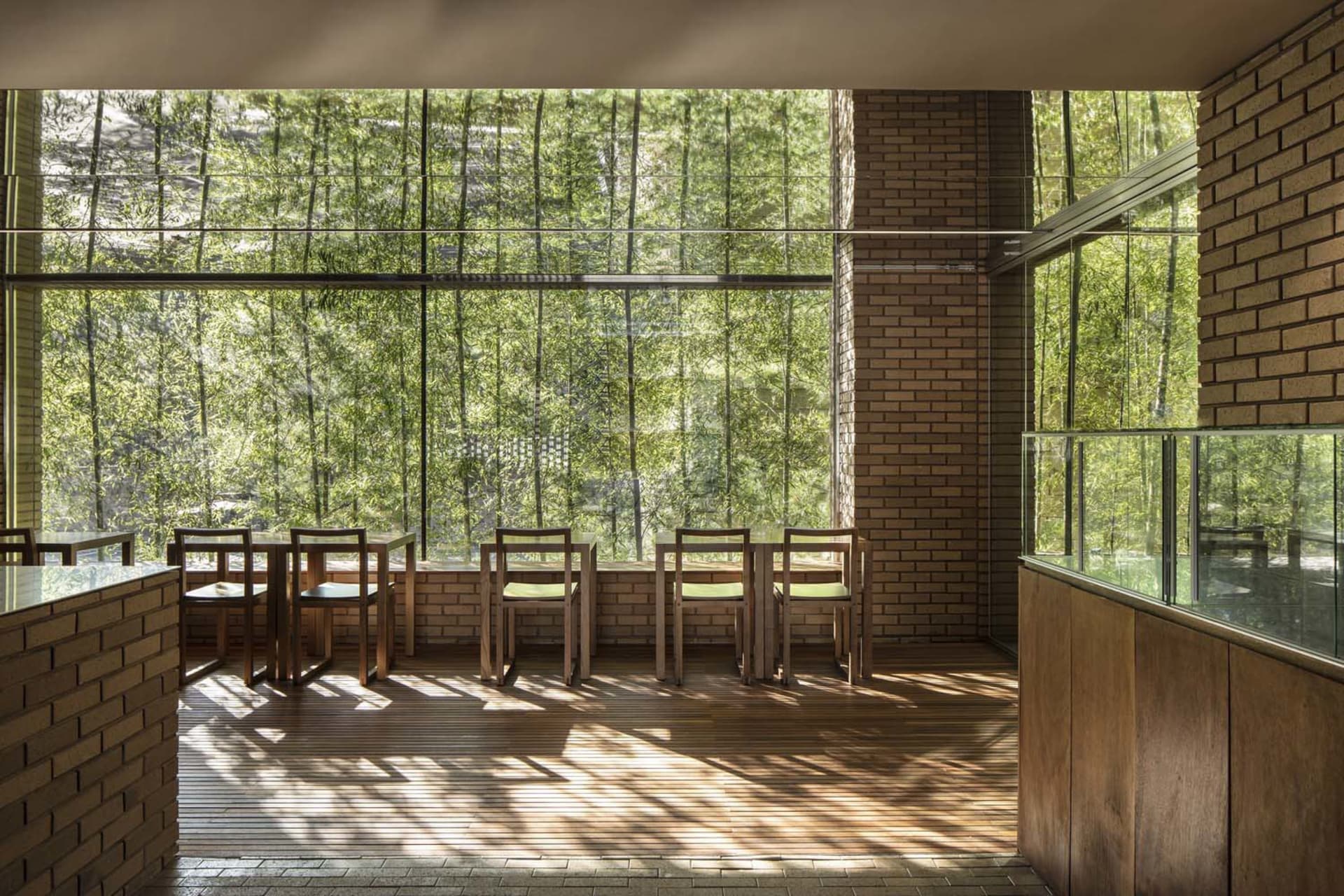 A modern coffee shop interior featuring brick walls, glass walls, and wooden furniture.