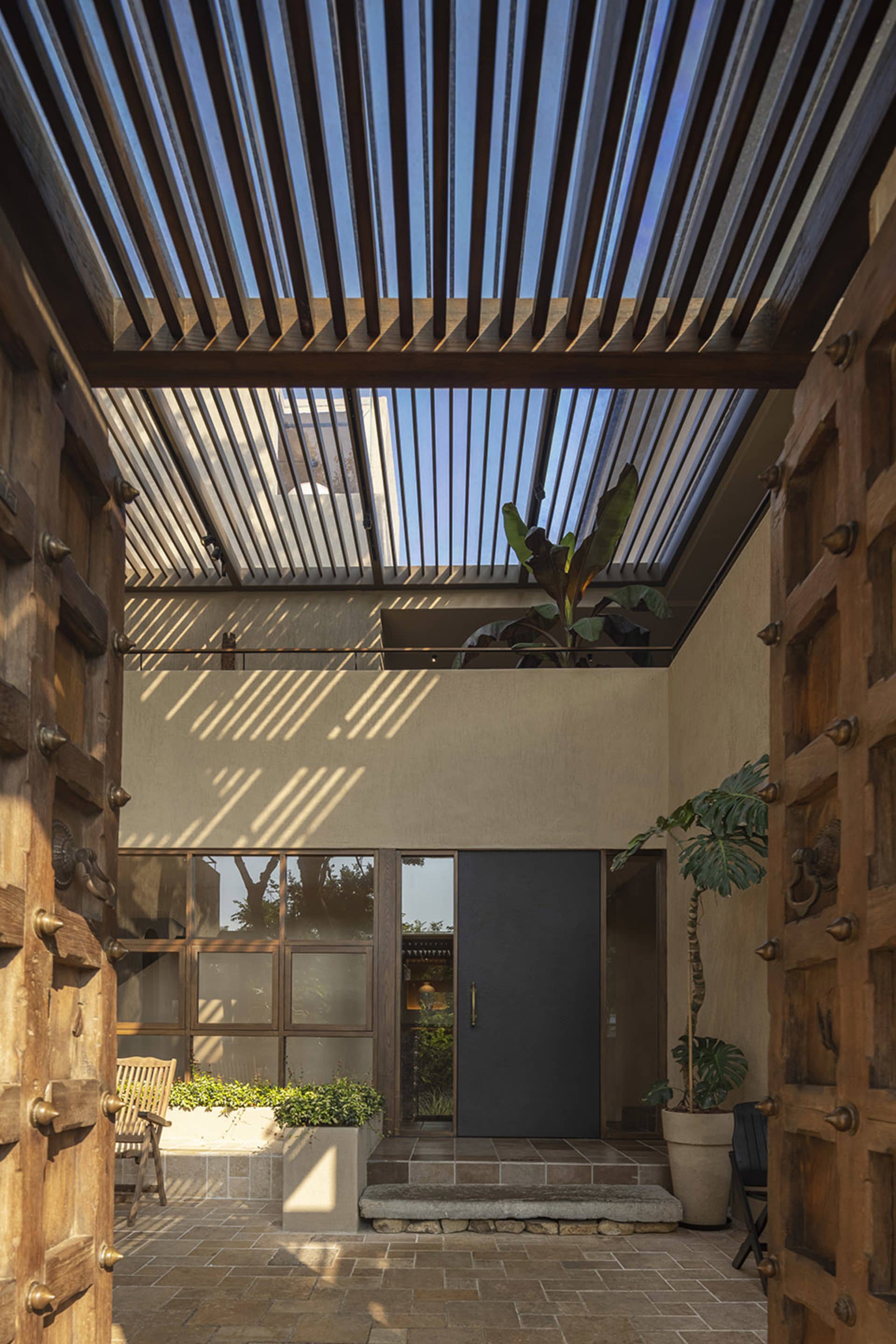 A modern entrance courtyard with concrete walls and potted plants under a wooden trellis roof.