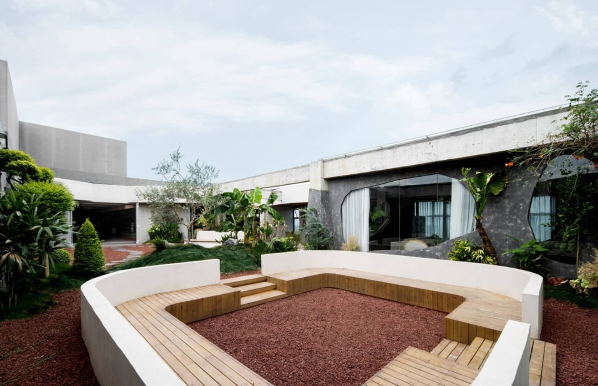A modern residential garden featuring concrete, wooden seating, and gravel ground.