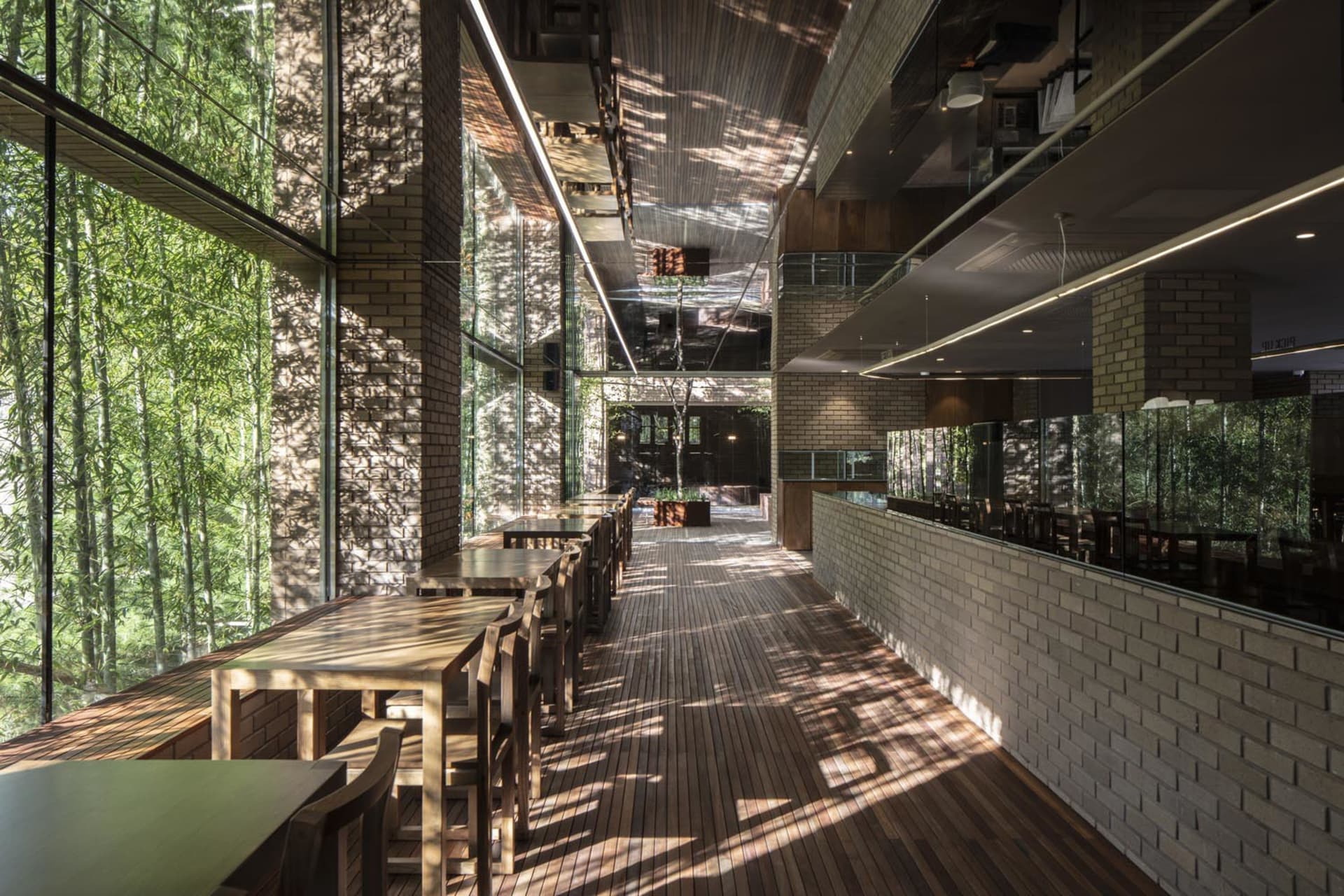 Modern restaurant interior with wooden tables and chairs, brick walls, and large windows