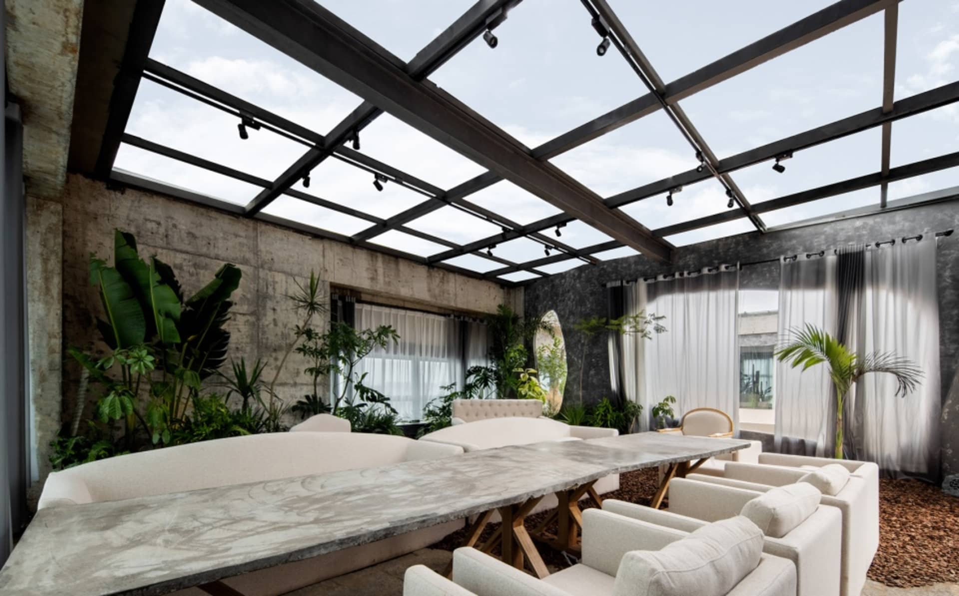 An industrial lounge area with a large concrete table, white upholstered chairs, and glass and concrete details.