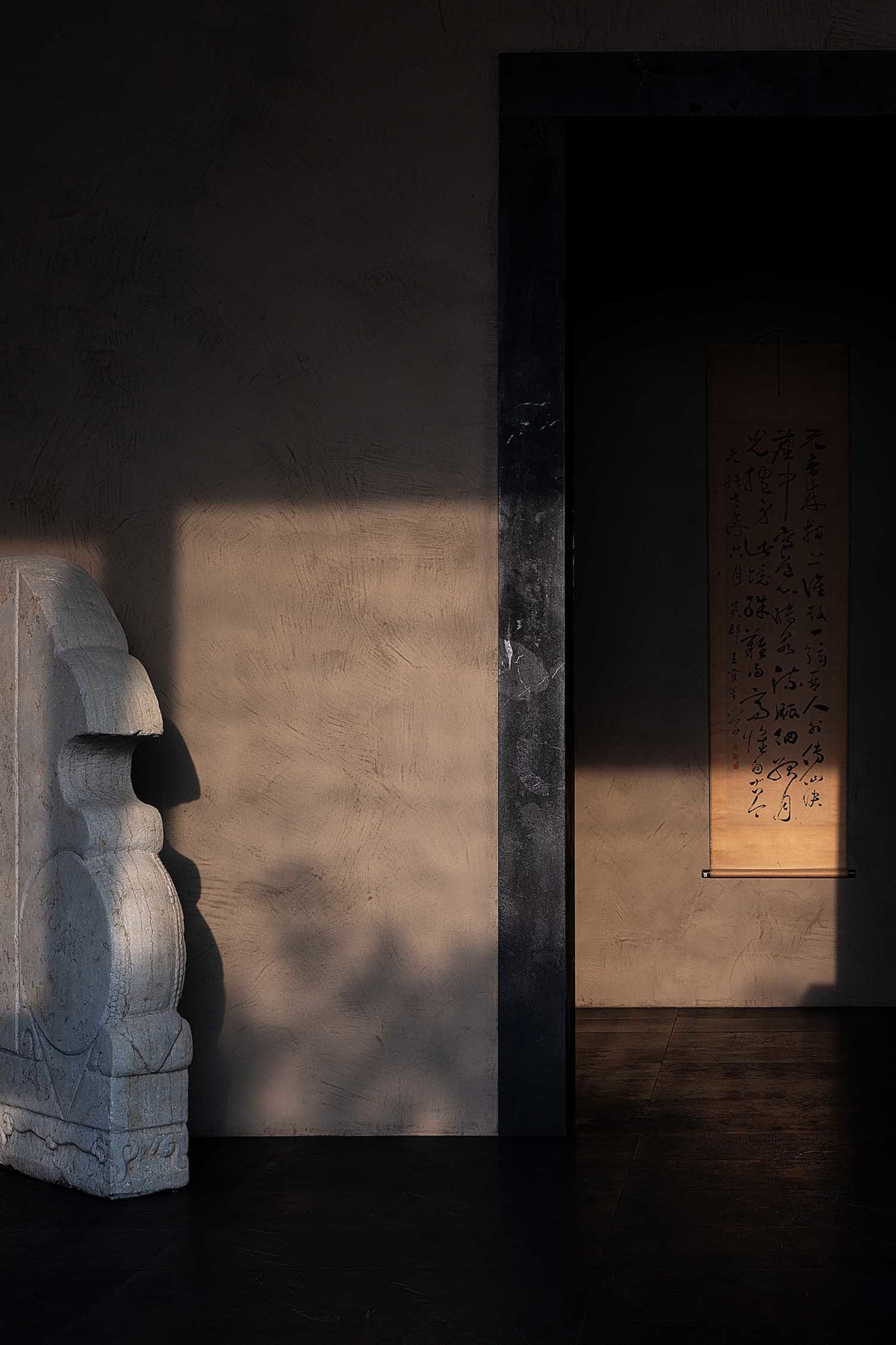 A minimalist bedroom decorated with a large concrete sculpture and a framed calligraphy scroll hanging on the wall.